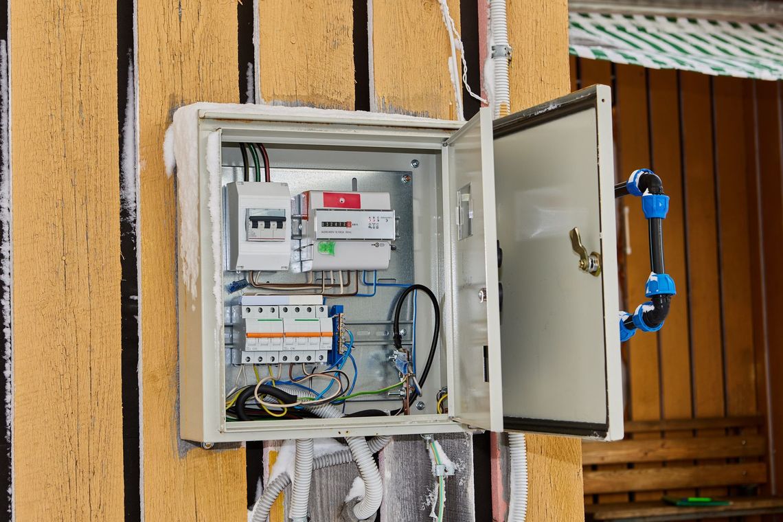 Open electrical control panel mounted on a wooden post, with wiring and blue cable connectors visible.