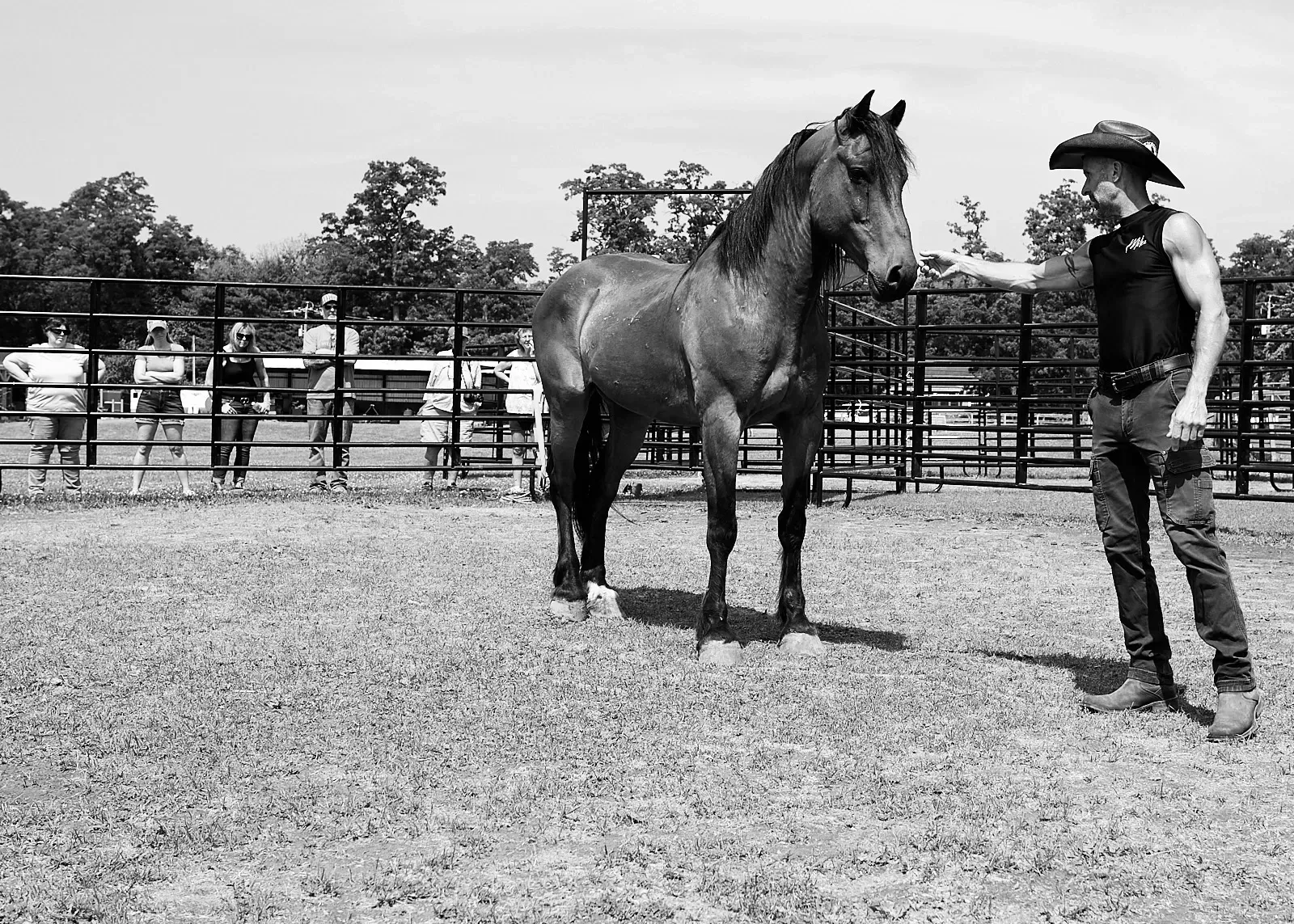 A man in a cowboy hat is petting a horse in a black and white photo.