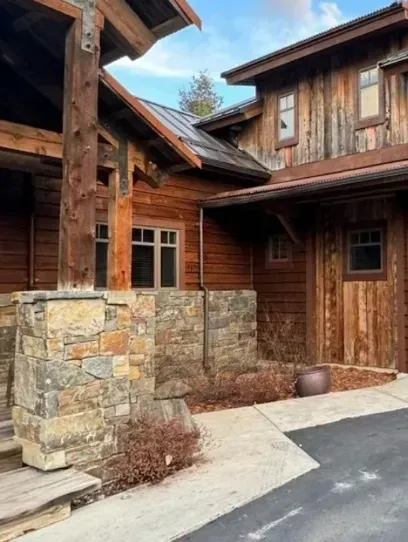 Rustic, wood-paneled house with stone columns, windows, and a driveway.