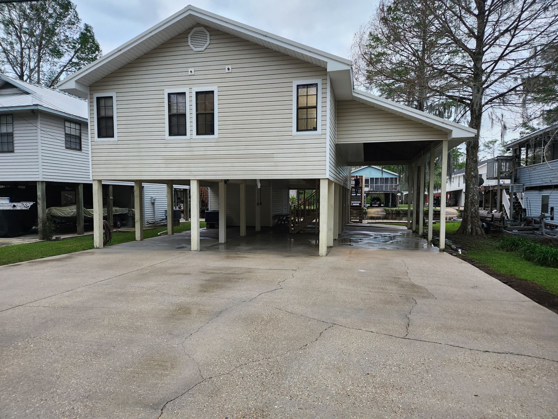 Elevated two-story house with light siding and a carport over a concrete driveway.