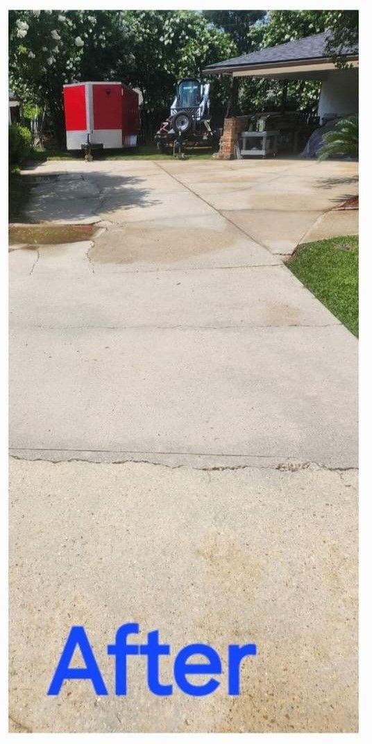 Concrete driveway after cleaning, with a red trailer, trees, and house visible in the background. 
