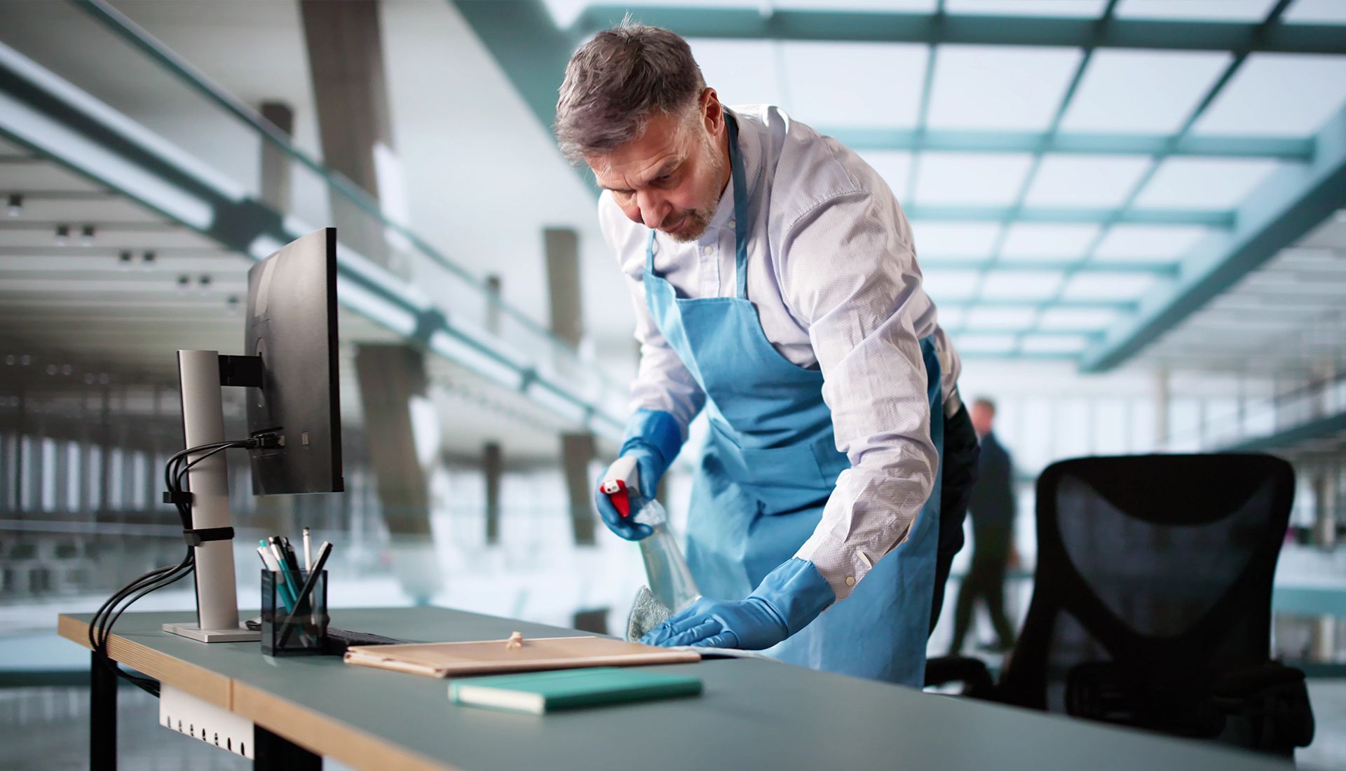 Man in gloves and apron cleaning an office desk.
