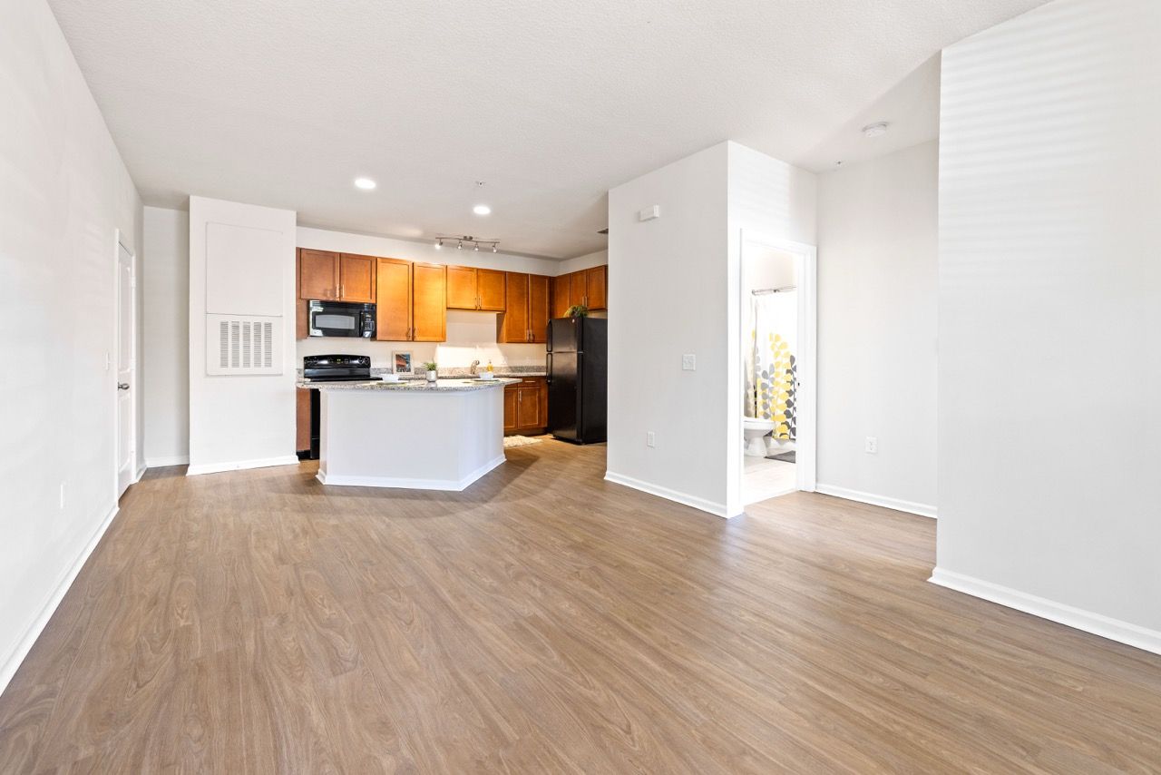 Open-concept apartment interior with kitchen island, wood cabinets, and laminate flooring.