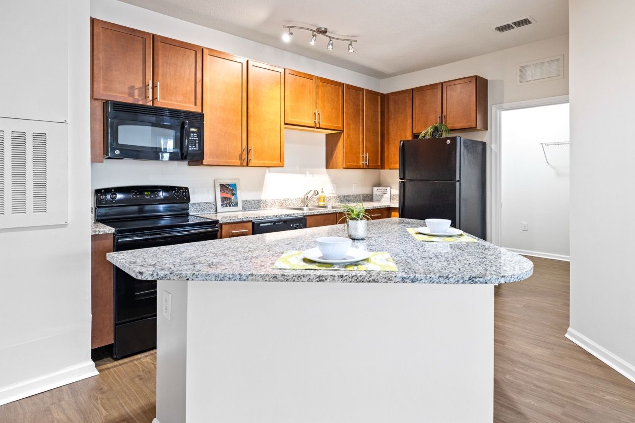 Kitchen in an apartment with granite countertops, wooden cabinets, and black appliances atThe Hawthorne.