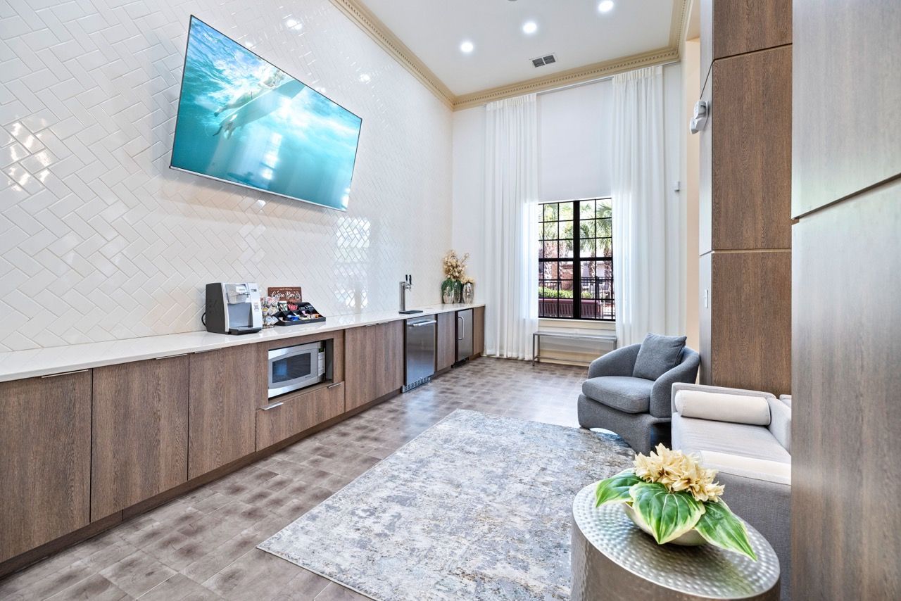 Interior community lounge with kitchenette, TV, and seating by a large window at The Hawthorne.