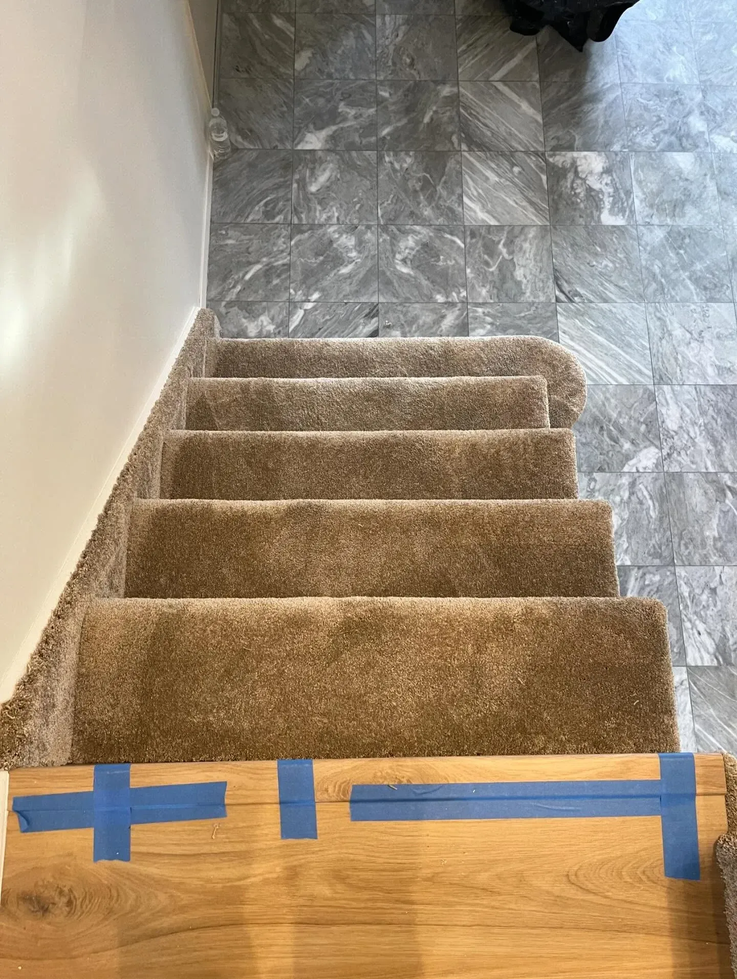 Carpeted staircase with blue tape marking the bottom step near a tiled landing