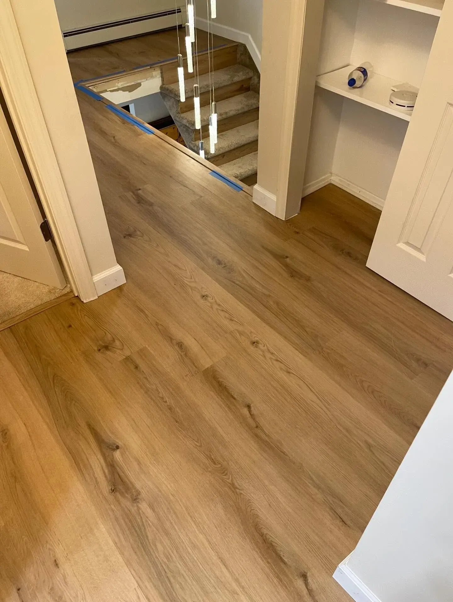 Wood-look floor in a hallway with stairs, built-in shelves, and a bathroom vanity in the background.