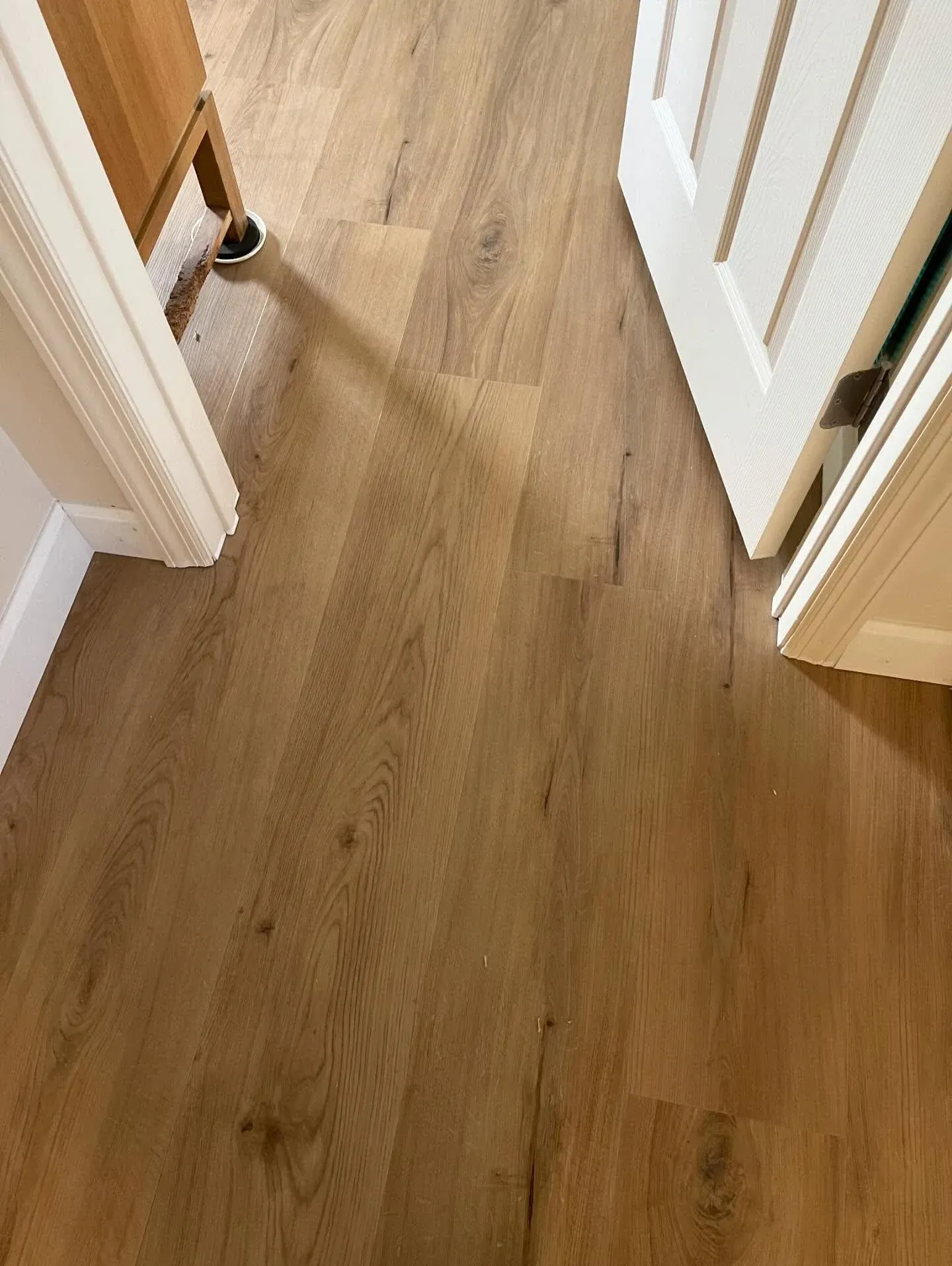 Wooden hallway floor between open white doorways, with a small chair leg visible on the left.
