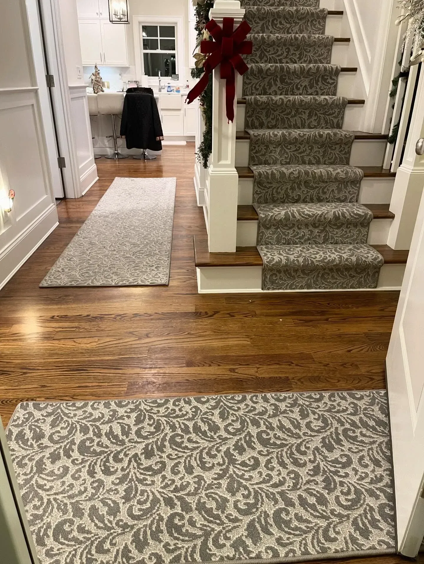 Entryway with hardwood floor, patterned rugs, and a staircase decorated with a red bow.