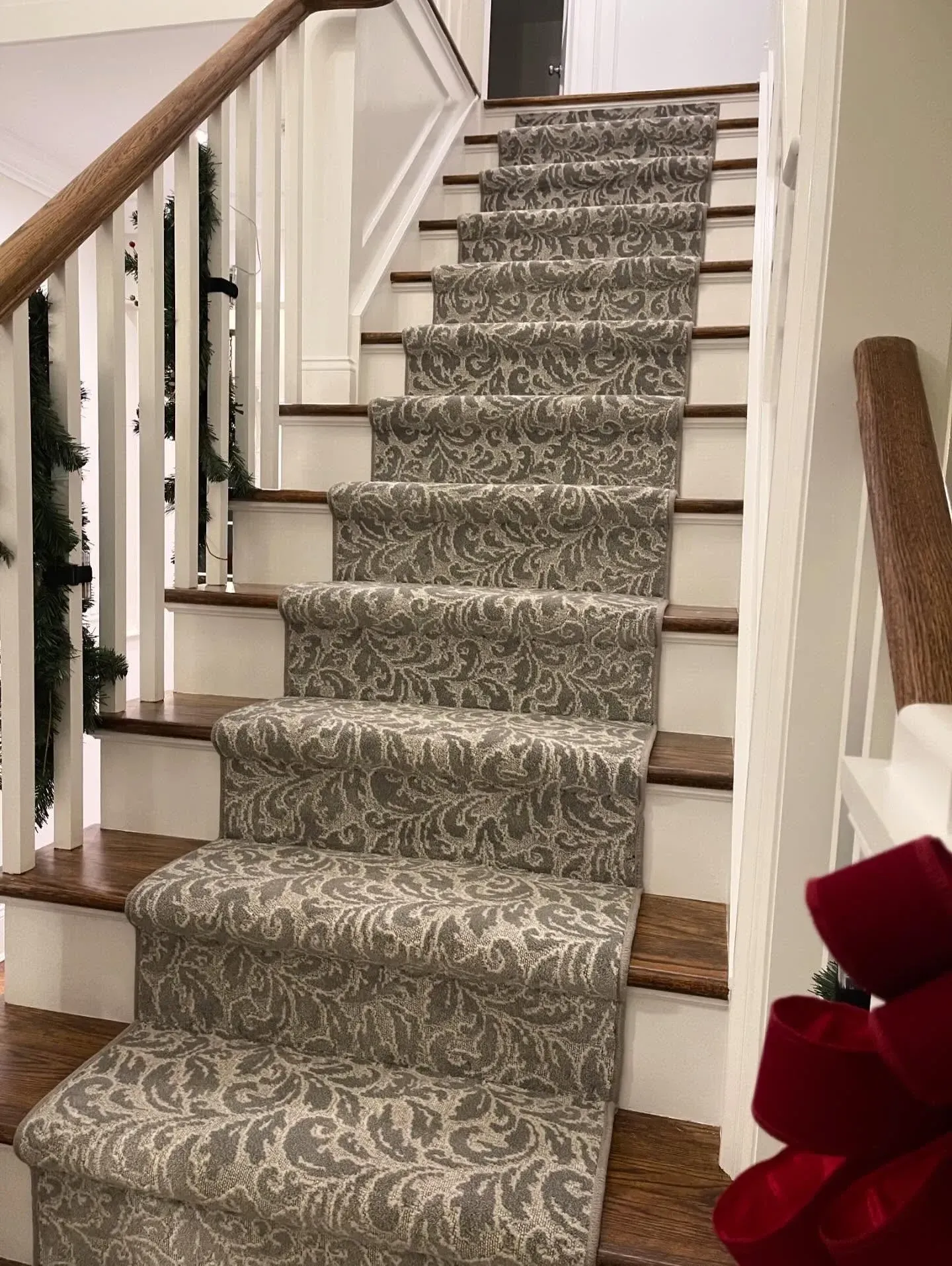 Carpeted staircase with wooden railings and white trim, viewed from the bottom, with a red bow on the right.