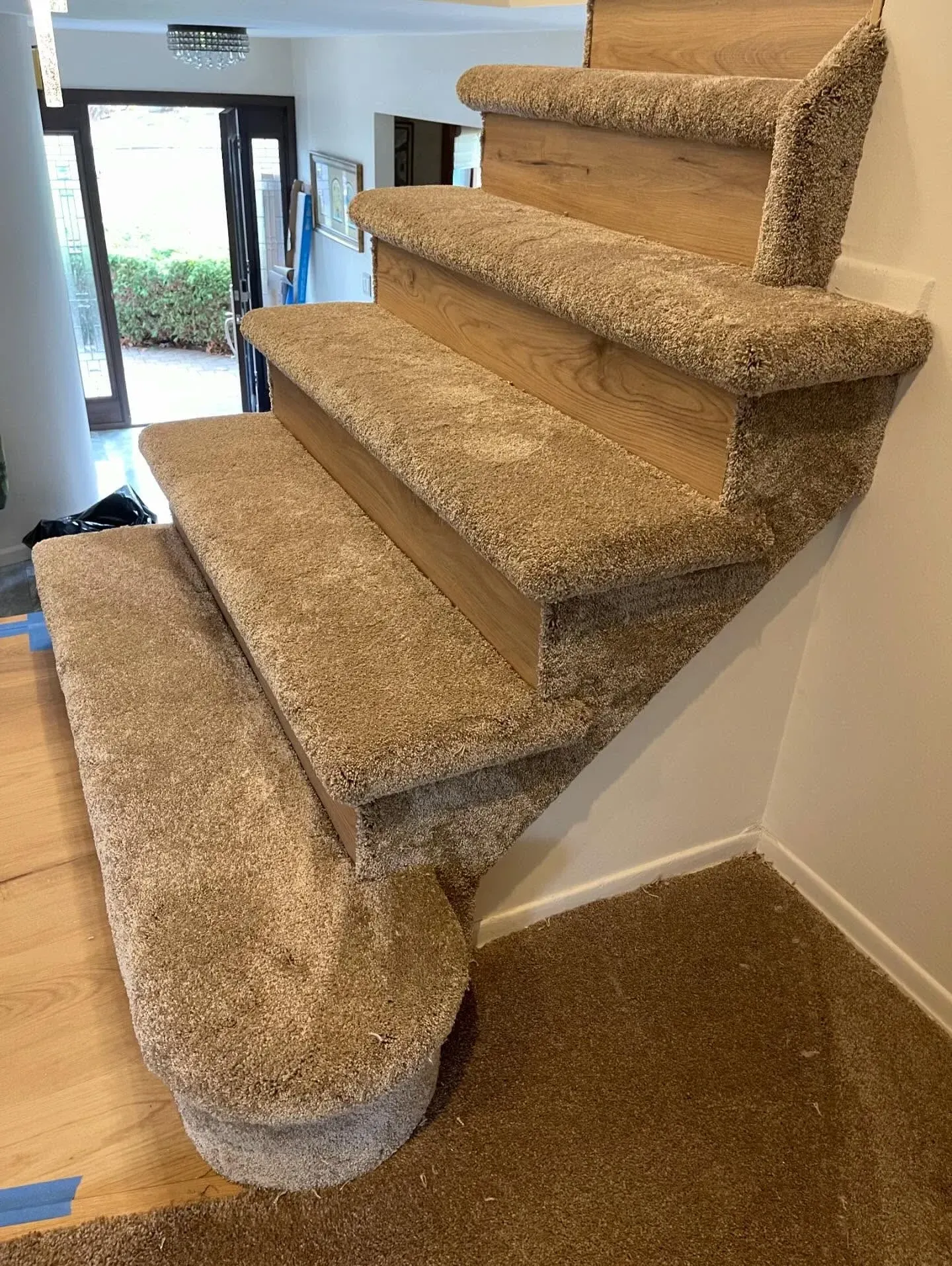 Carpeted curved staircase with tan steps and a light-colored wall beside a wooden floor.