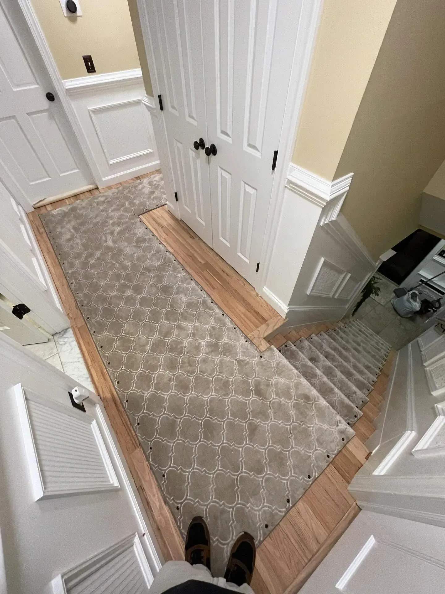 Hallway with patterned runner rug, white closet doors, and a pair of shoes visible at the bottom.