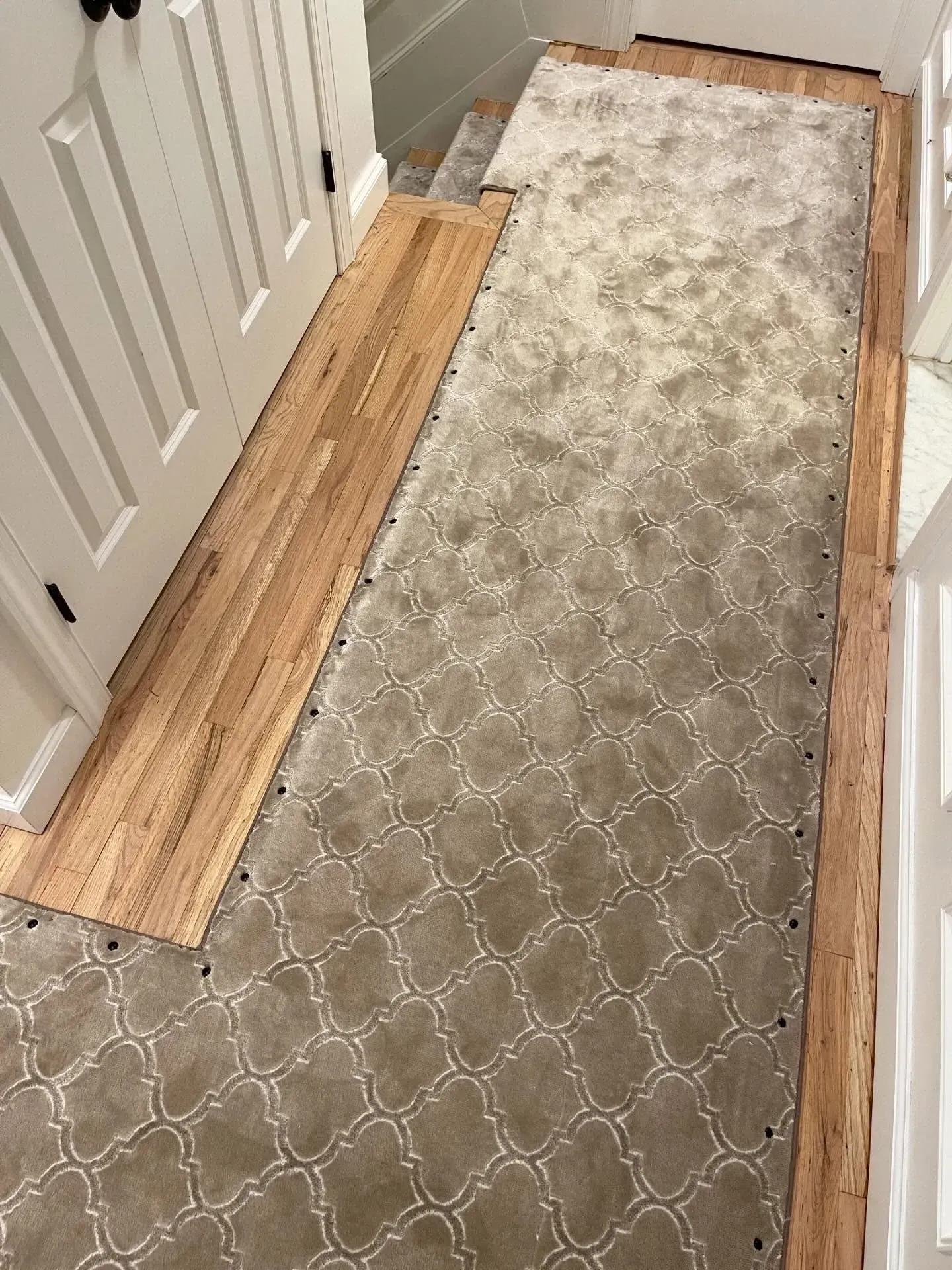 Narrow hallway with a carpet runner over unfinished wood flooring beside white closet doors.