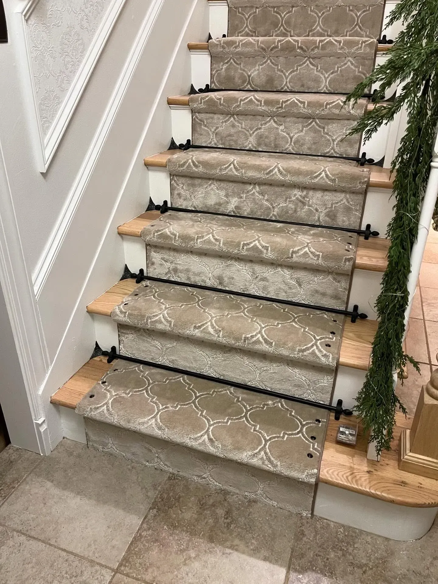 Carpeted indoor staircase with patterned runner, white walls, and holiday greenery on the right.