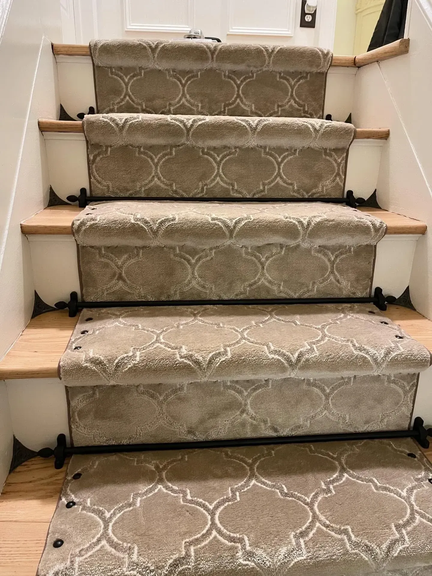 Carpeted staircase with patterned beige runner and black stair rod accents