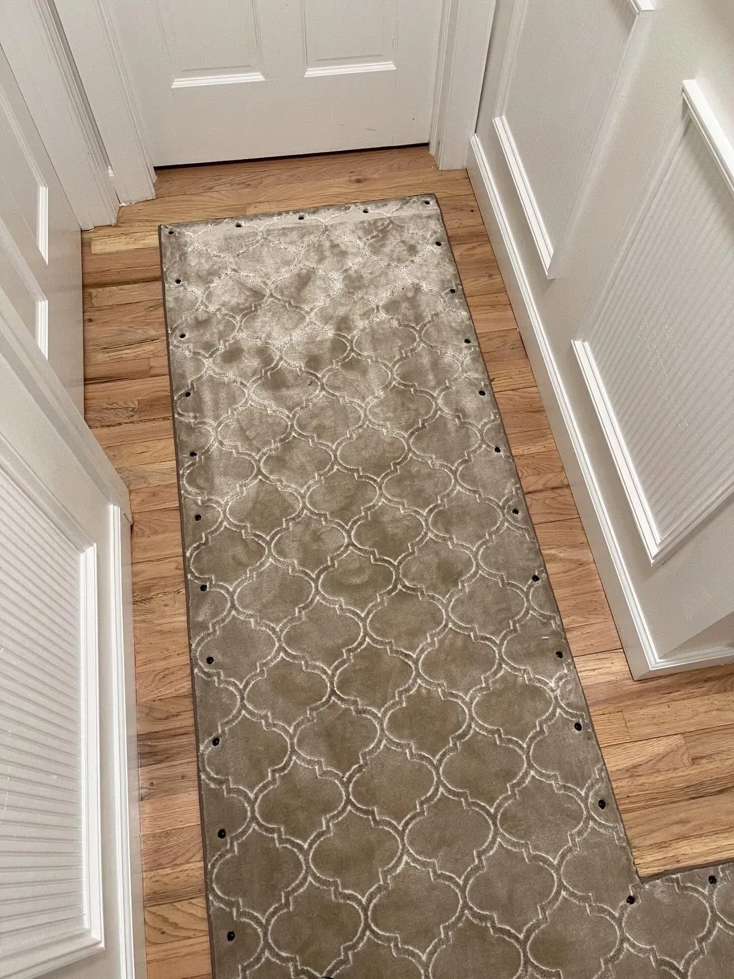 Narrow hallway with light wood flooring, white paneled doors, and a beige patterned runner rug