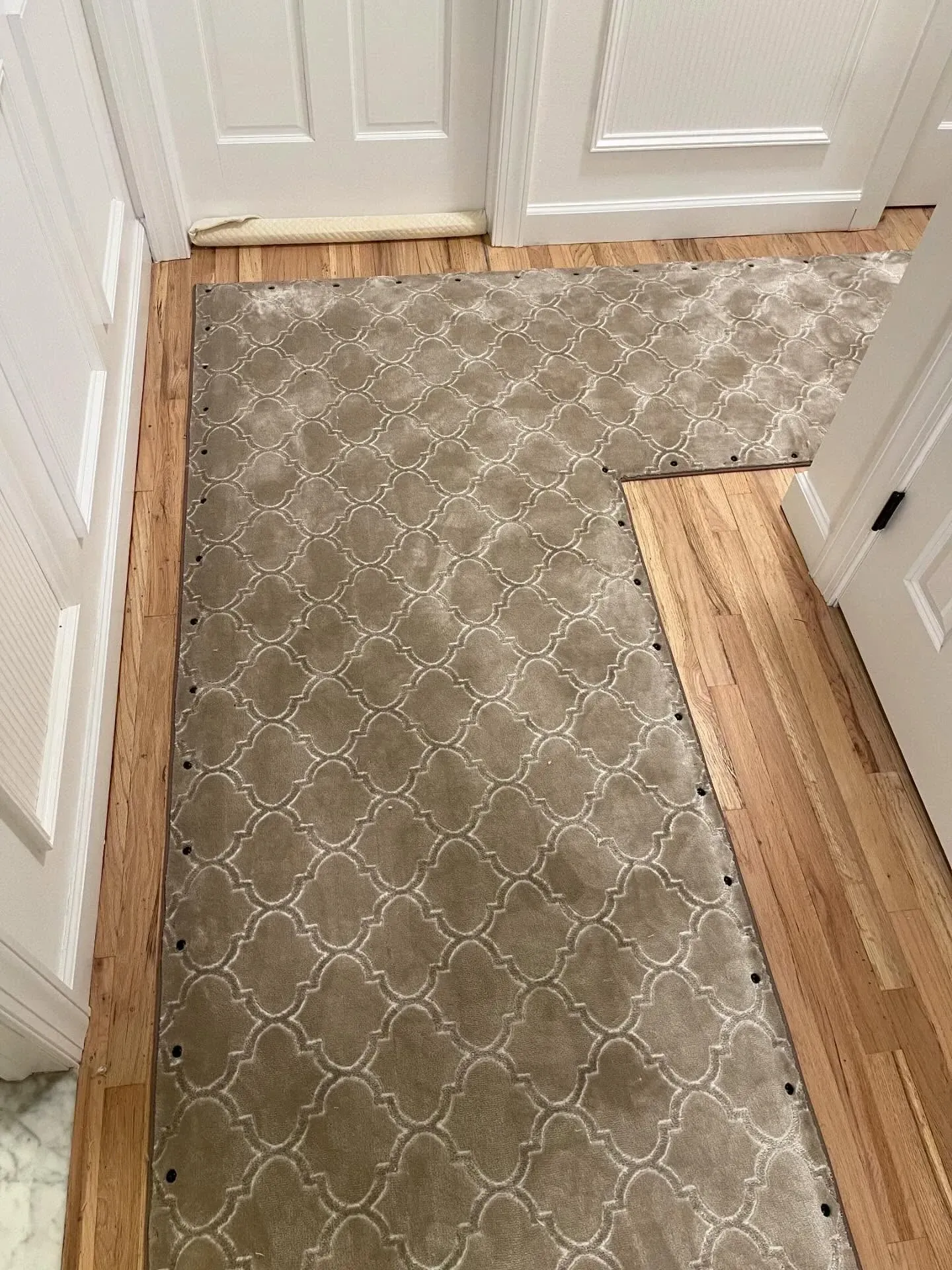 Carpeted hallway with wood flooring patches and baseboards near white doors