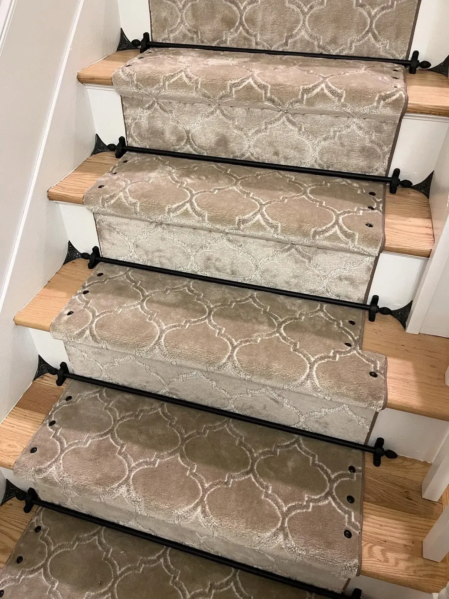 Carpet stair treads on wooden steps with black safety rods along a staircase