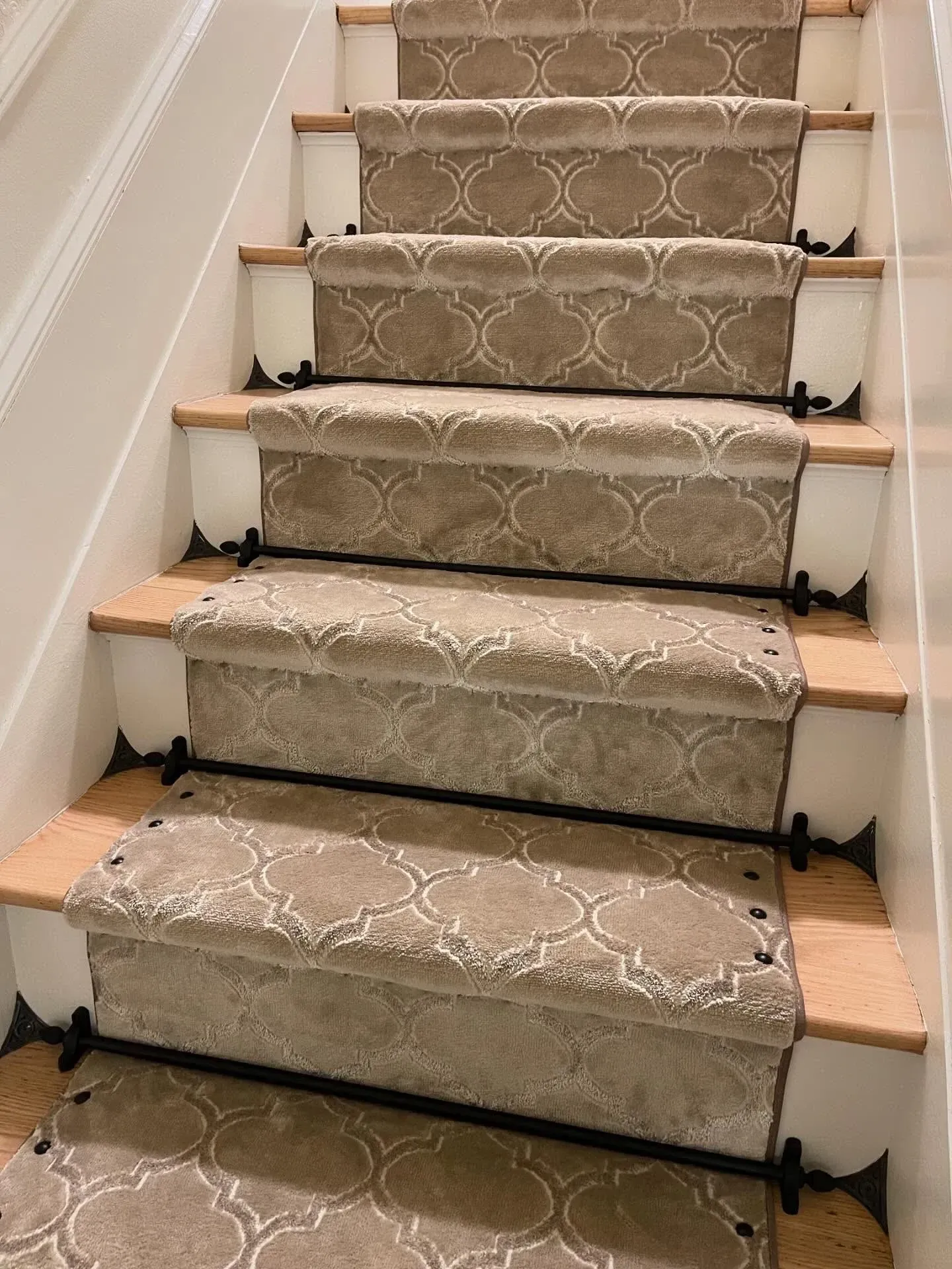 Carpeted staircase with beige patterned runner and black stair rods on white walls