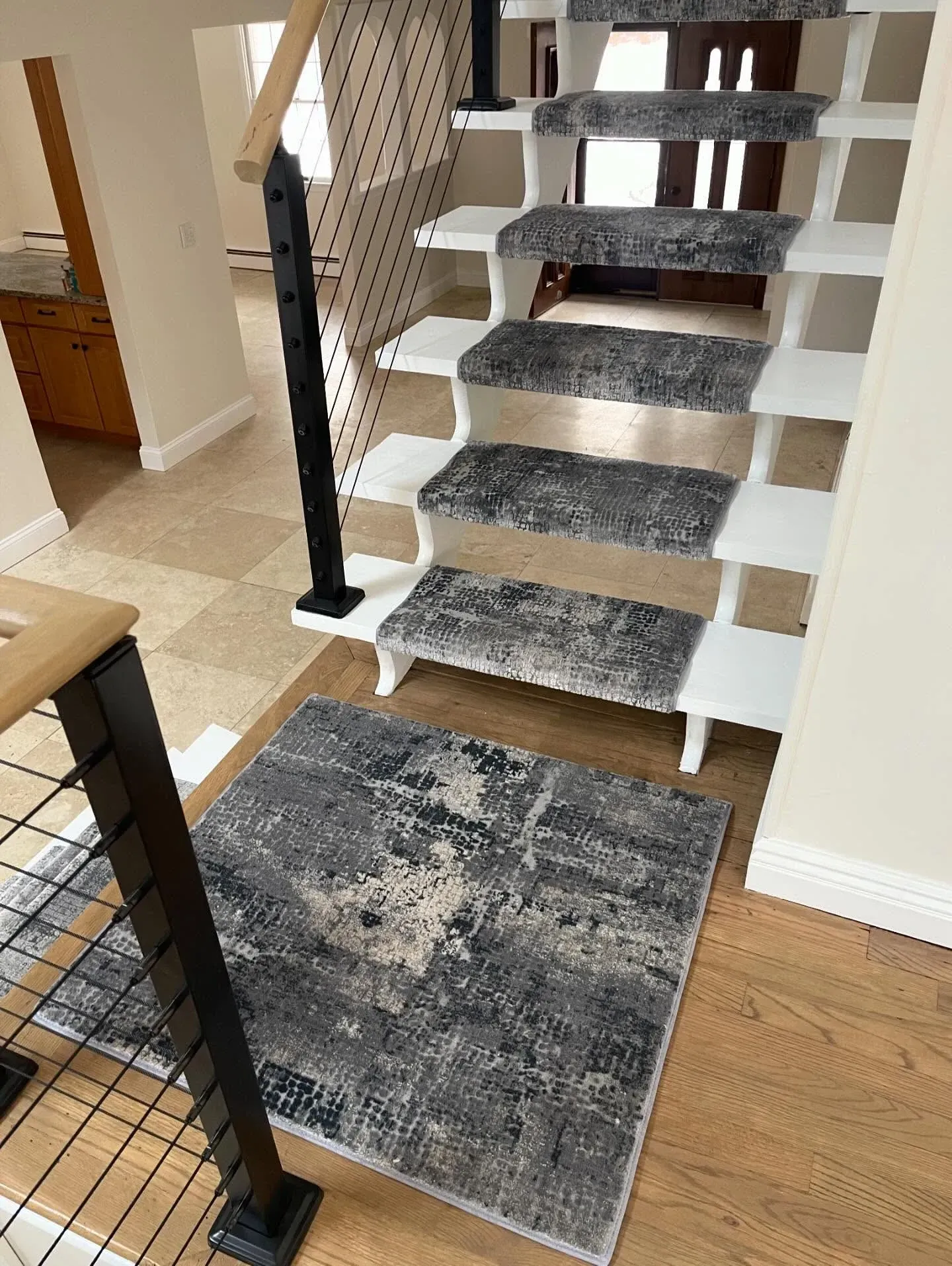 Indoor staircase with dark carpet runner and a gray rug at the bottom in a home entryway