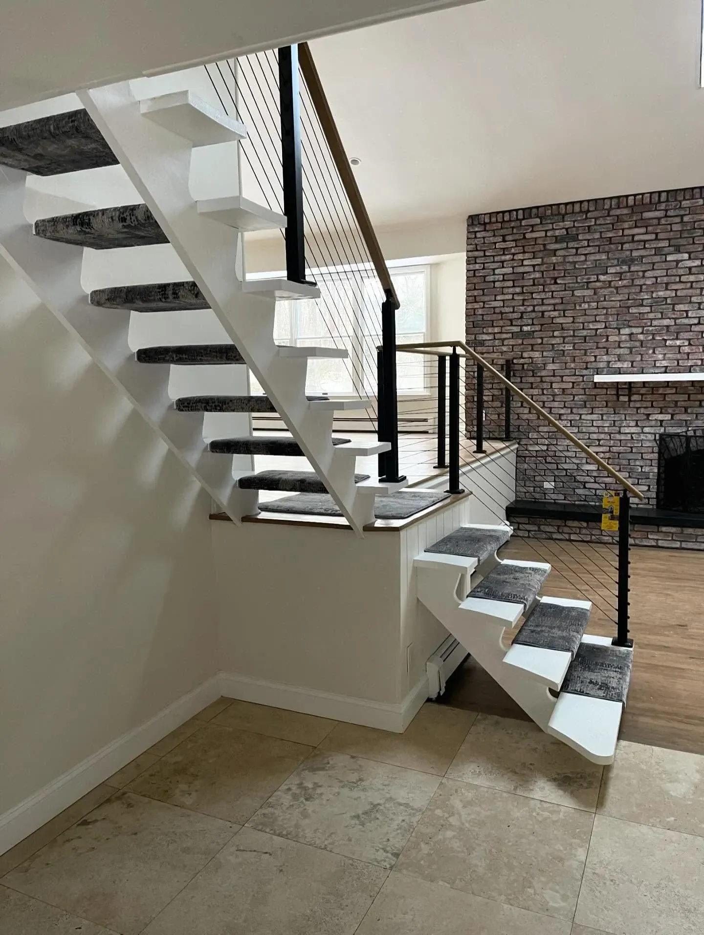 Spiral staircase with black railings in a modern interior, beside a brick accent wall and tiled floor.