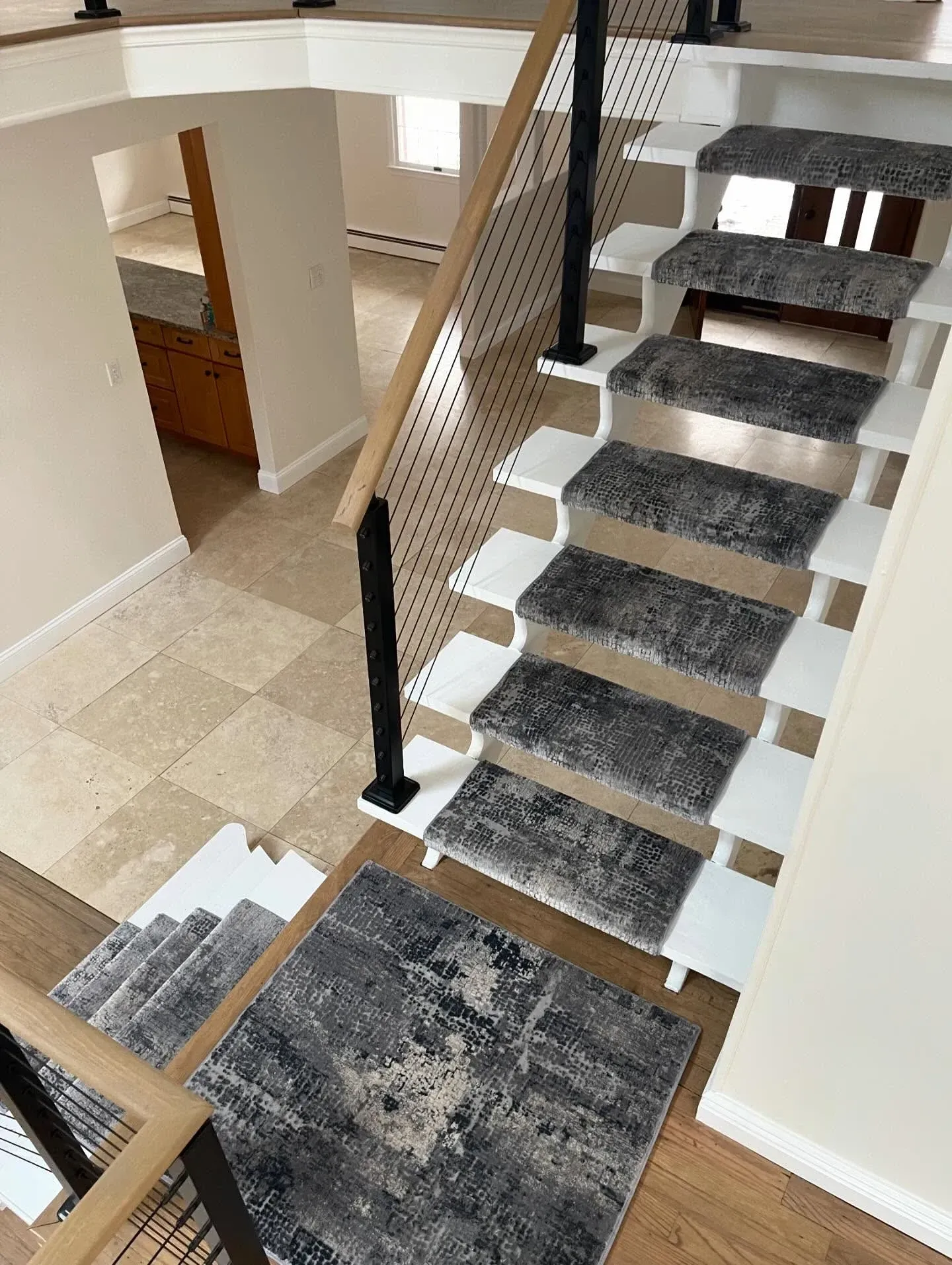 Modern staircase with gray carpeted steps, black railing, and light tile flooring in a bright interior.