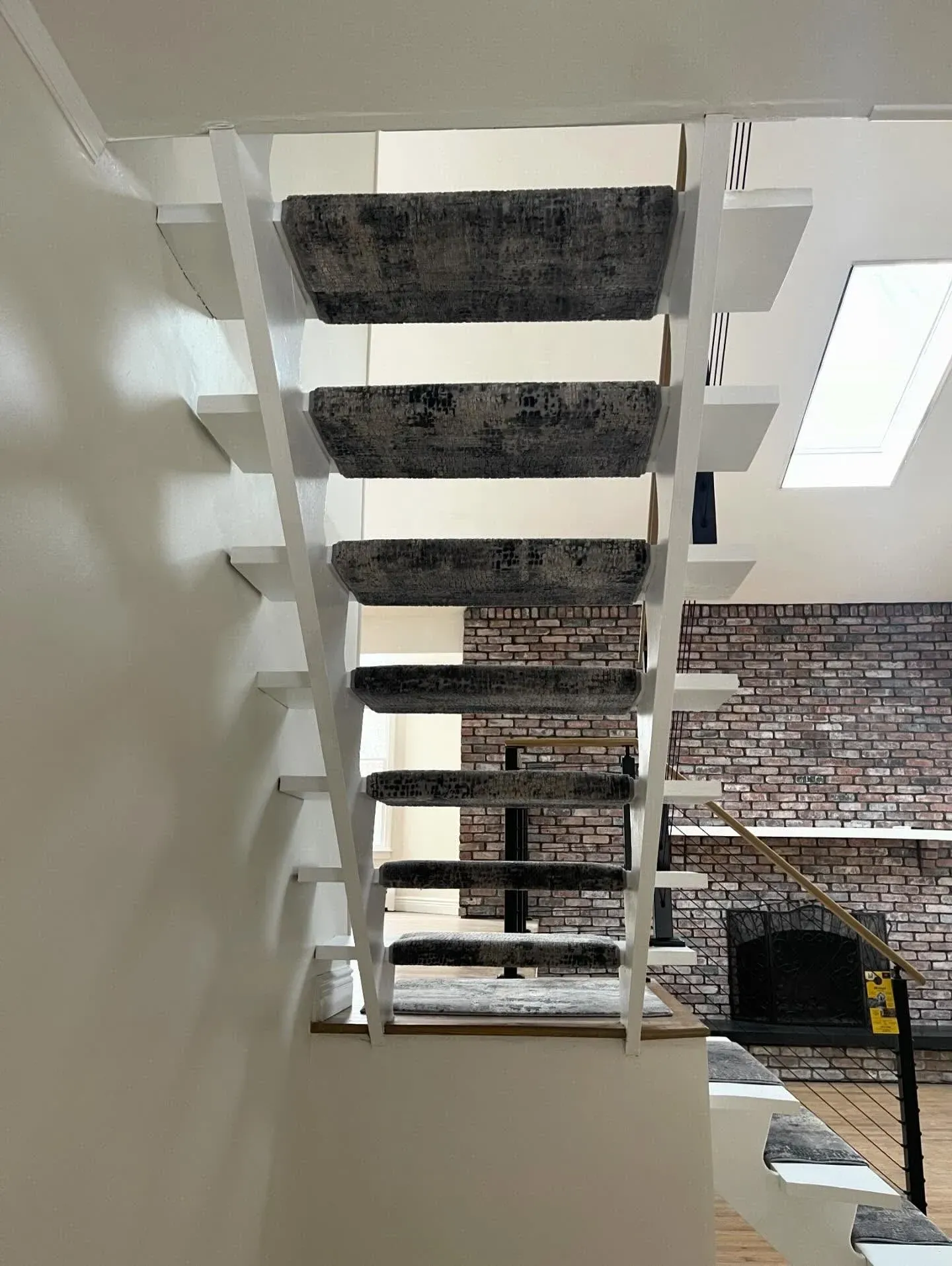 Looking up a white staircase with black carpet treads in a modern interior, beside a brick wall.