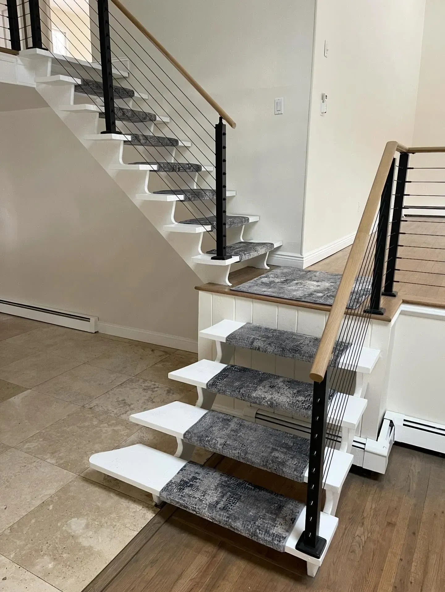 Interior staircase with carpeted steps, black railings, and white walls in a home hallway