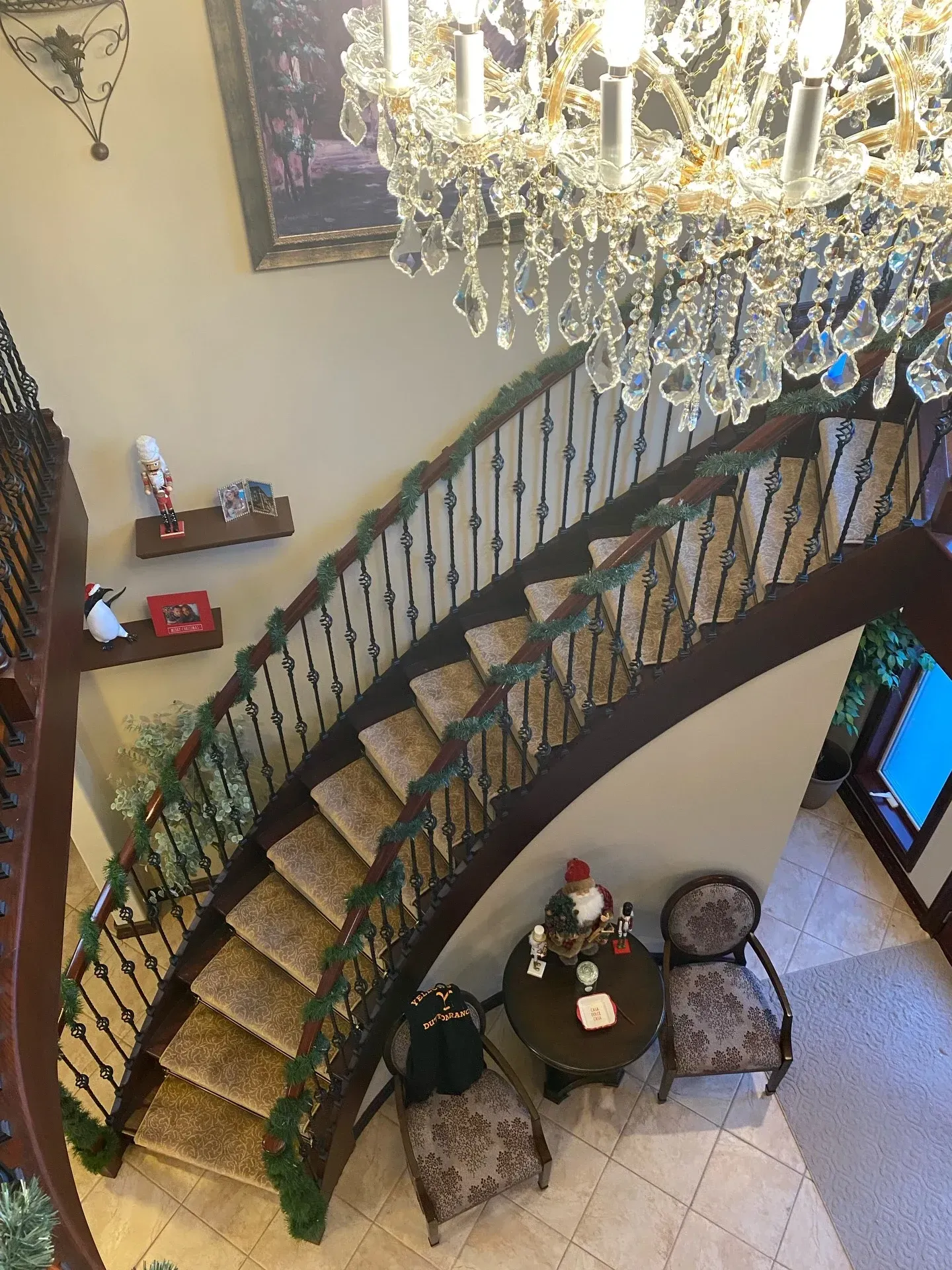 Elegant staircase with dark railings, crystal chandelier, and a small round table in a warmly lit foyer