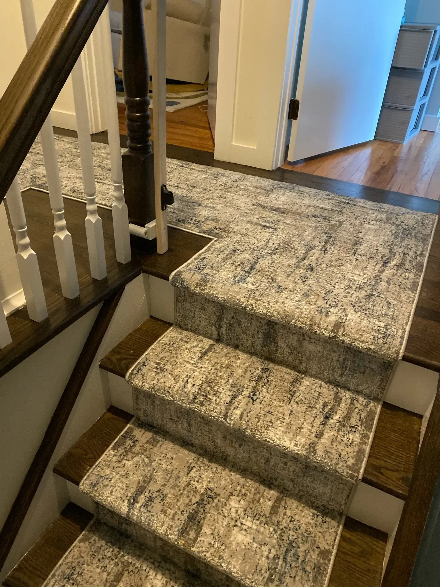 Carpeted indoor staircase with a small landing and white railing, leading to a hallway floor