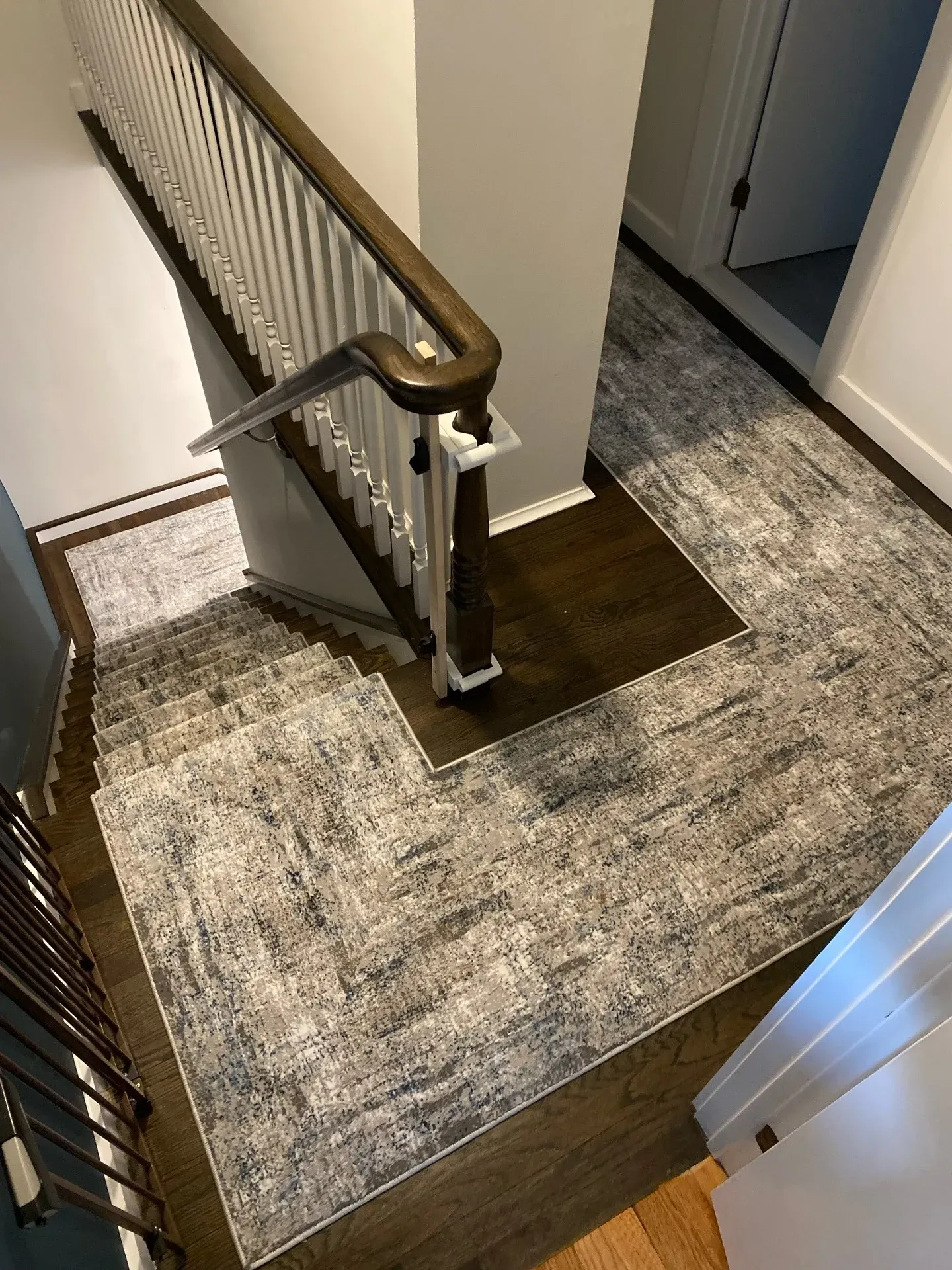 Stair landing with patterned carpet and white banister beside a hallway and doorway.