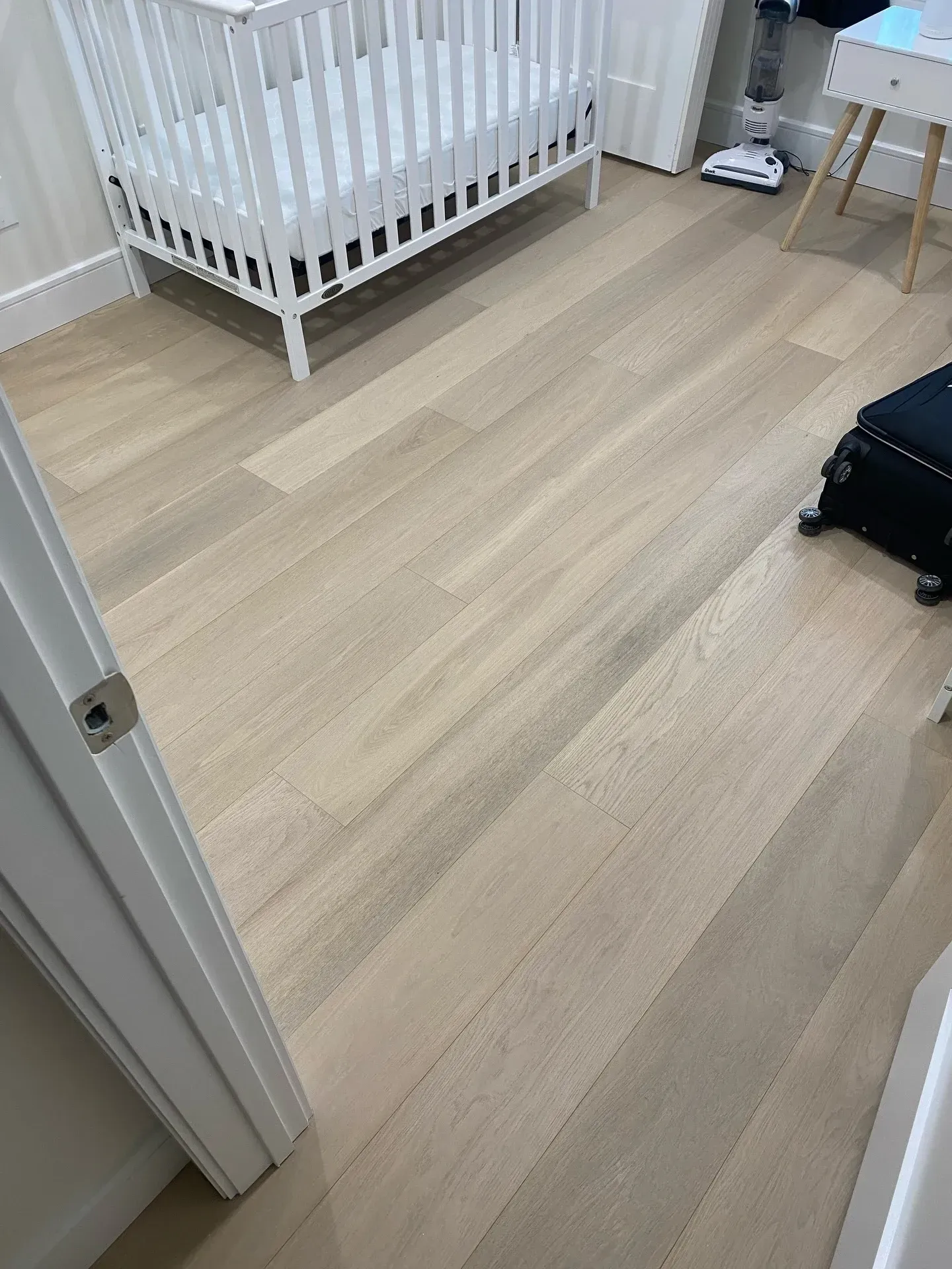Empty nursery with a white crib, light wood floor, and a small table in the corner.
