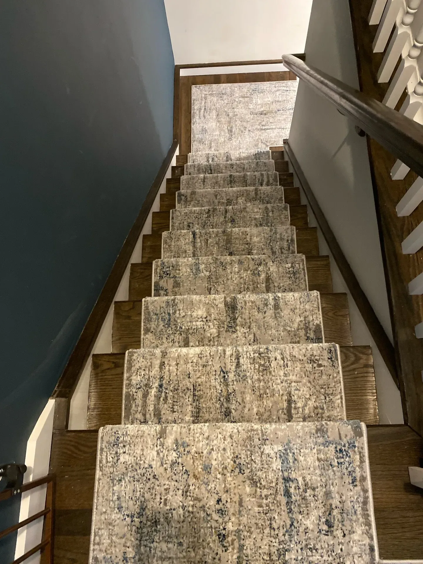 Carpeted staircase with dark railing and white balusters, viewed from the top looking down.