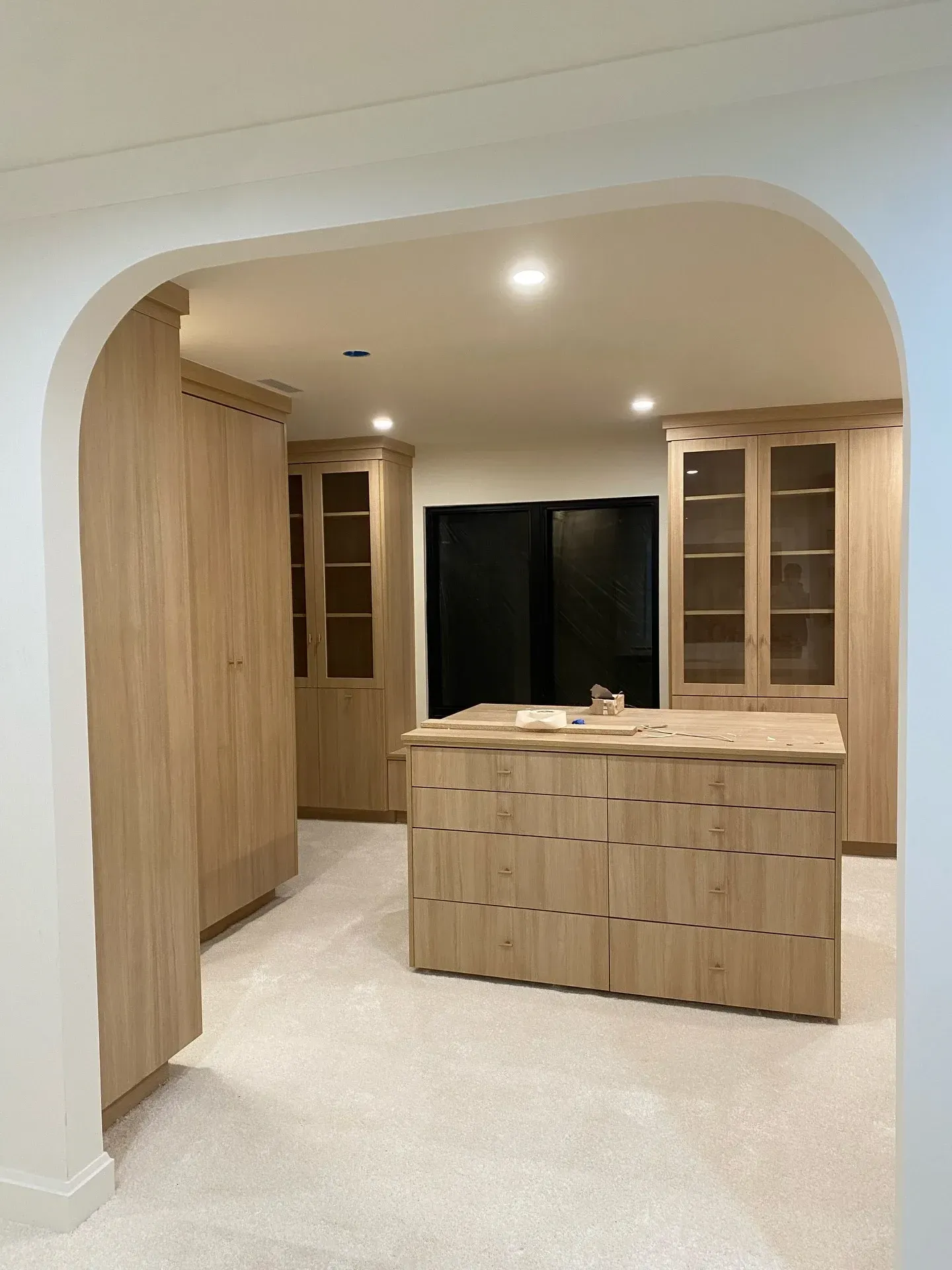 Bright wood kitchenette with cabinets and counter beneath a white arched doorway
