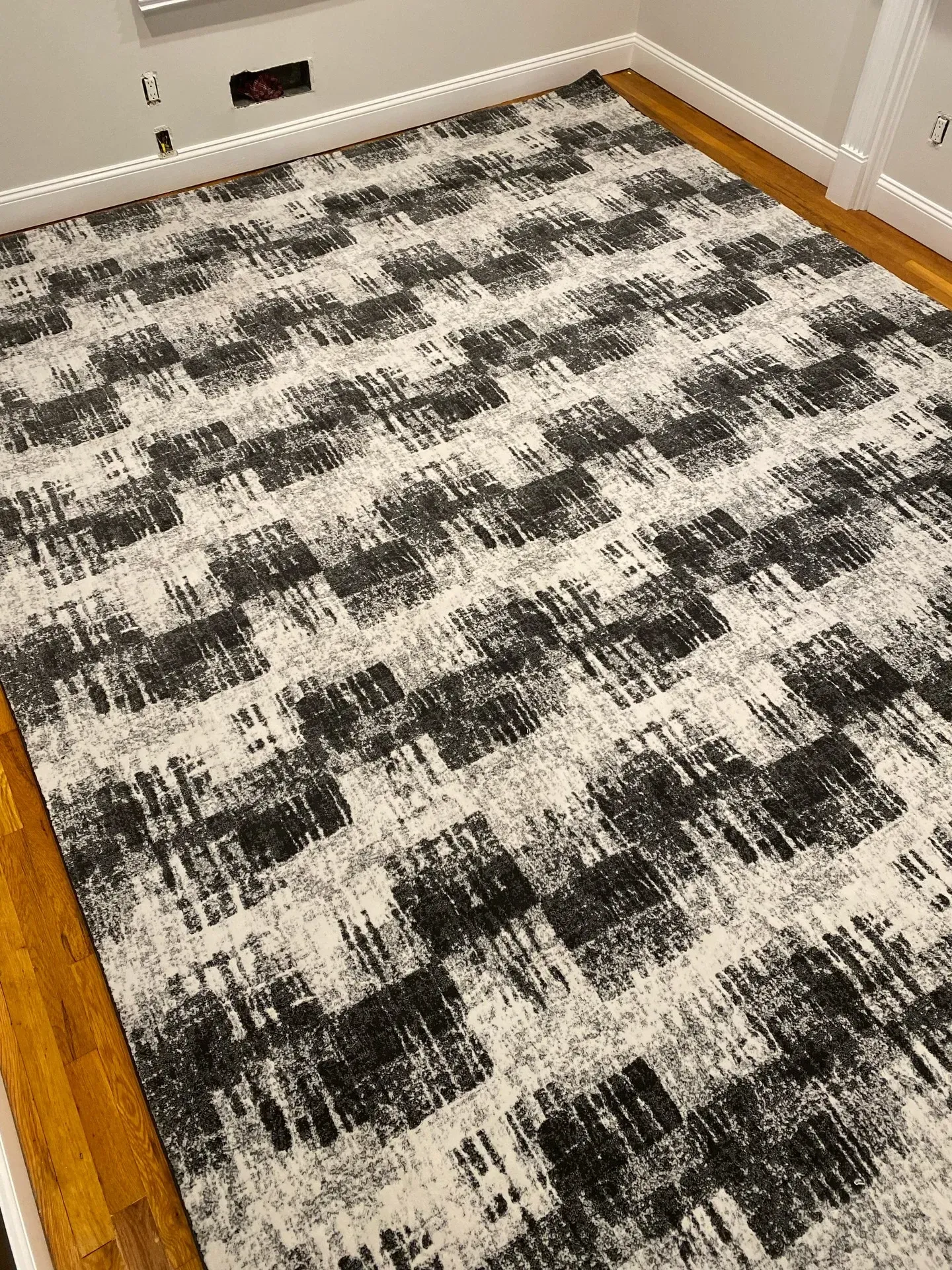 Black-and-white patterned area rug in a room with white baseboards and a wooden floor edge