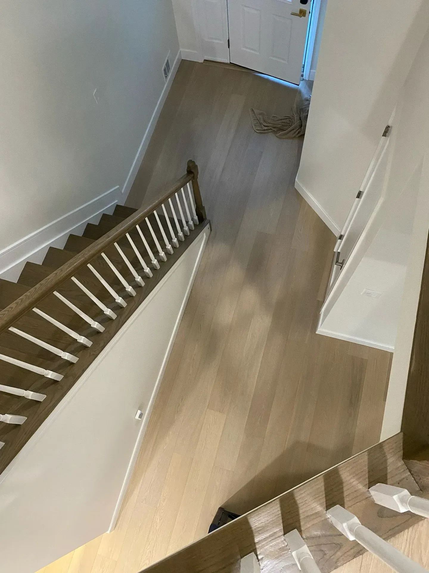 Staircase and hallway with light wood flooring and white walls, viewed from above.