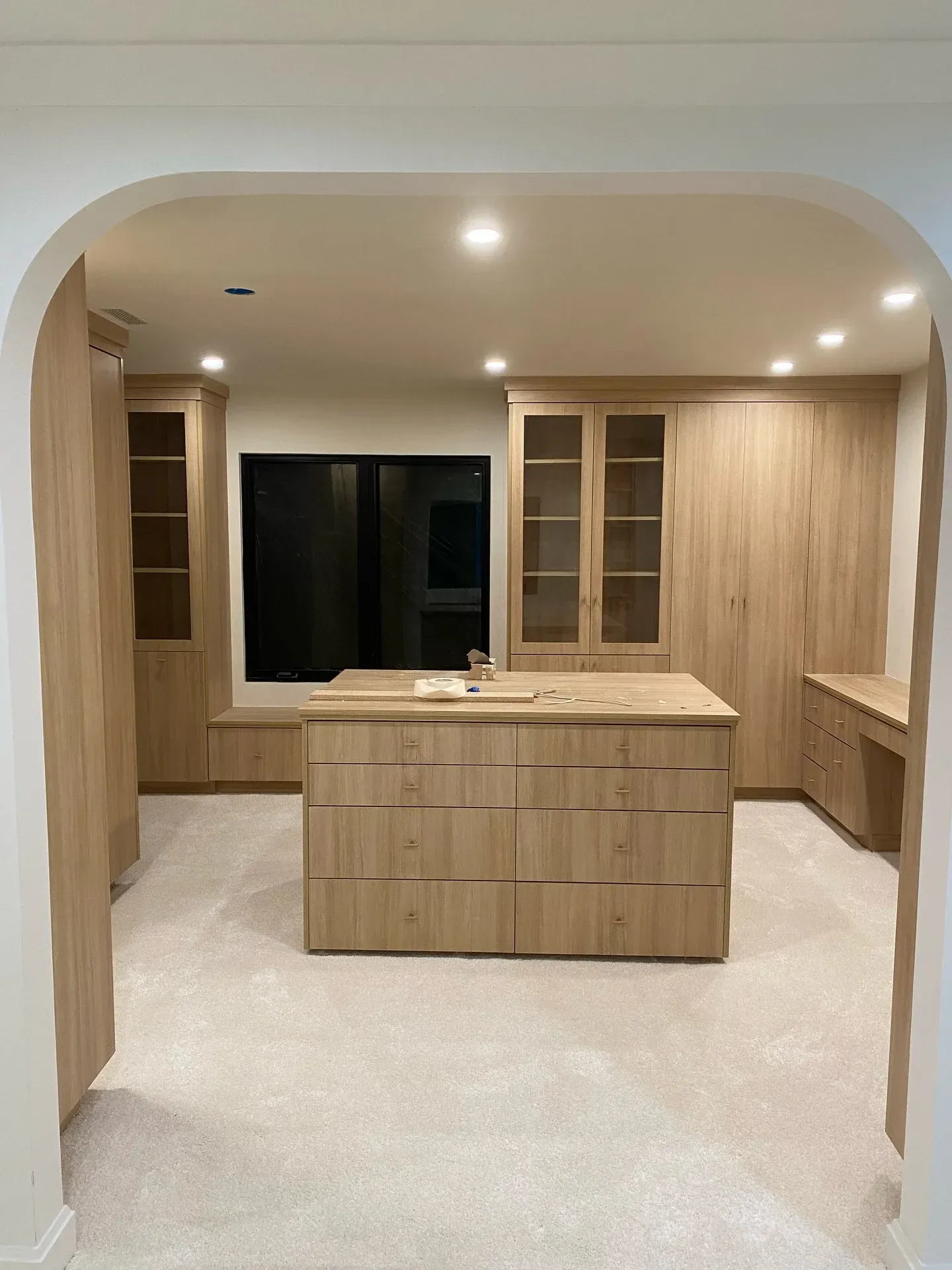 Modern kitchen with light wood cabinets, central island, and arched doorway.
