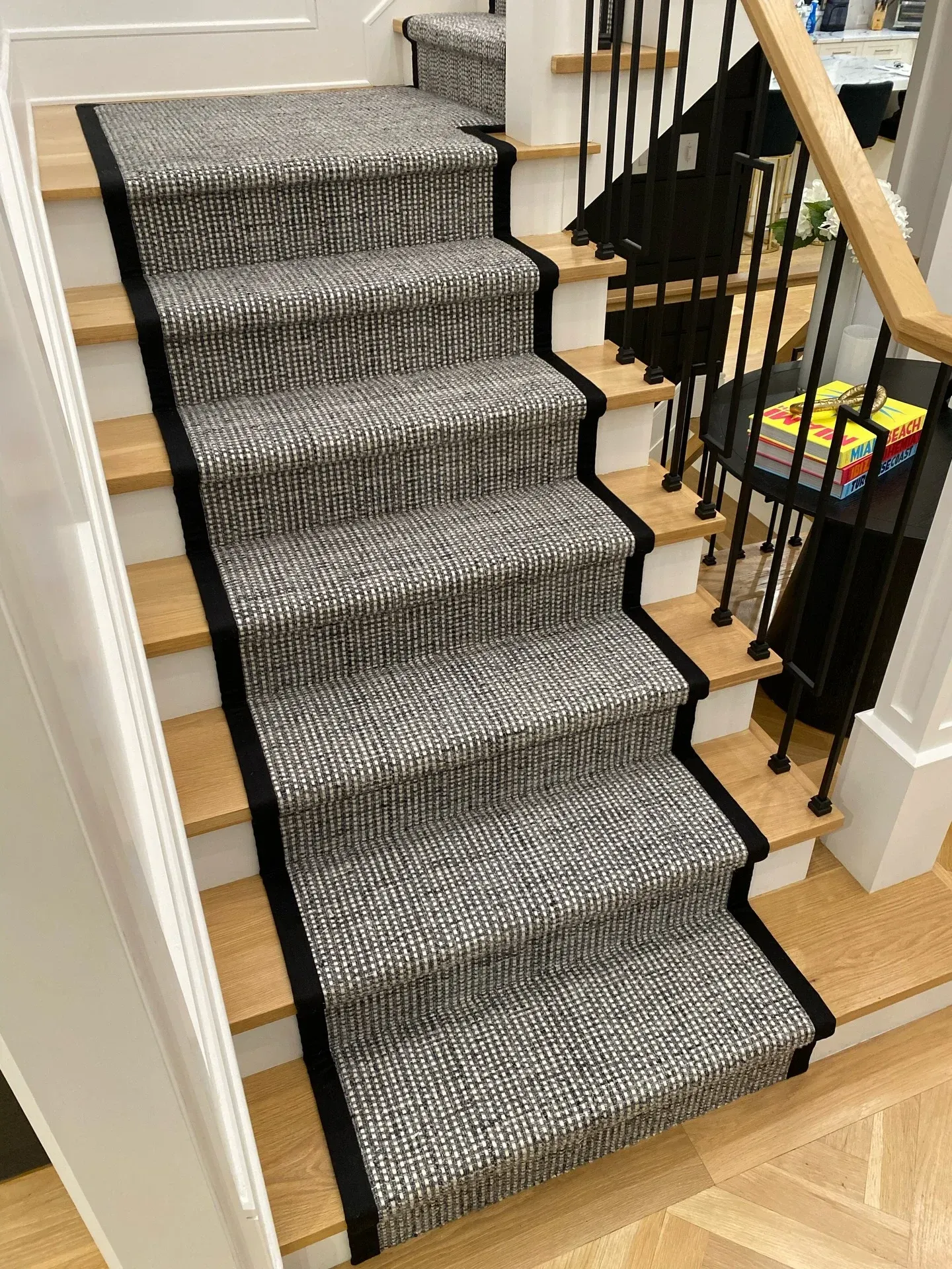 Carpeted staircase with black stair rods and wooden banister, viewed from the bottom indoors