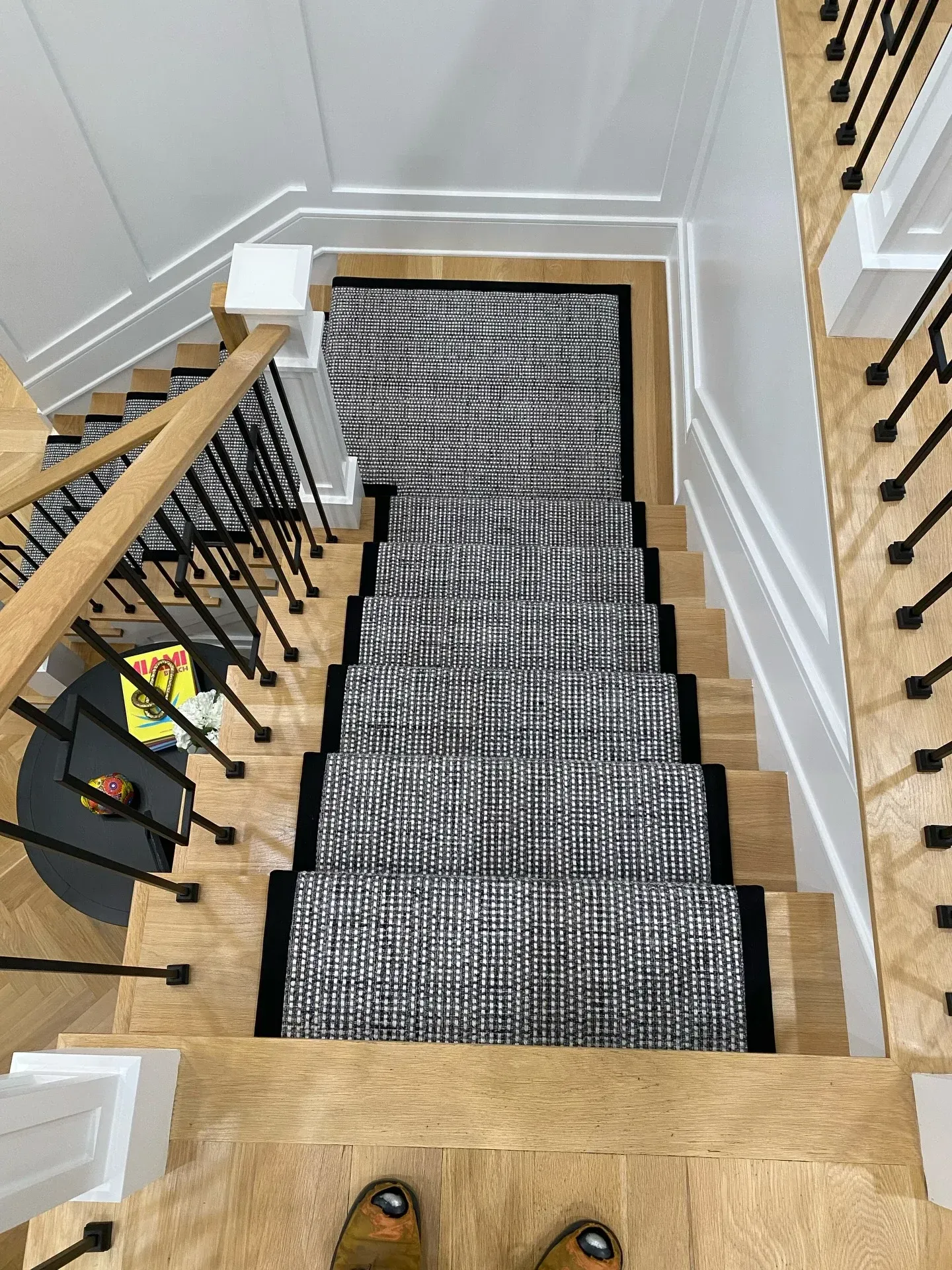 Staircase with black-and-white runner rug and wooden railings, viewed from the top down