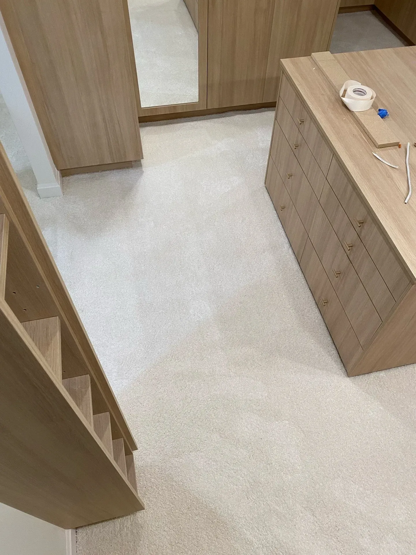 Wooden hallway with light carpet, a cabinet on the right, and a mirror at the far end.