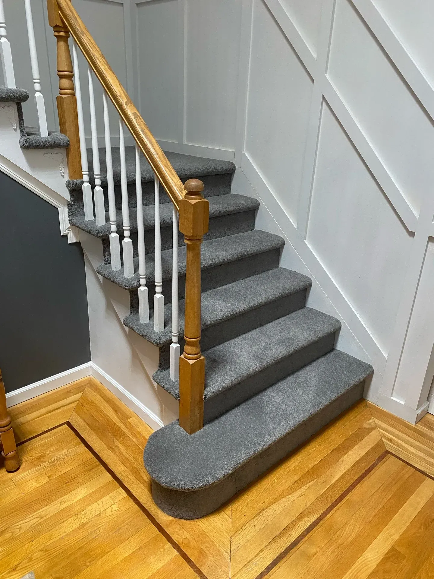 Carpeted staircase with wooden banister and white wall paneling in a home hallway