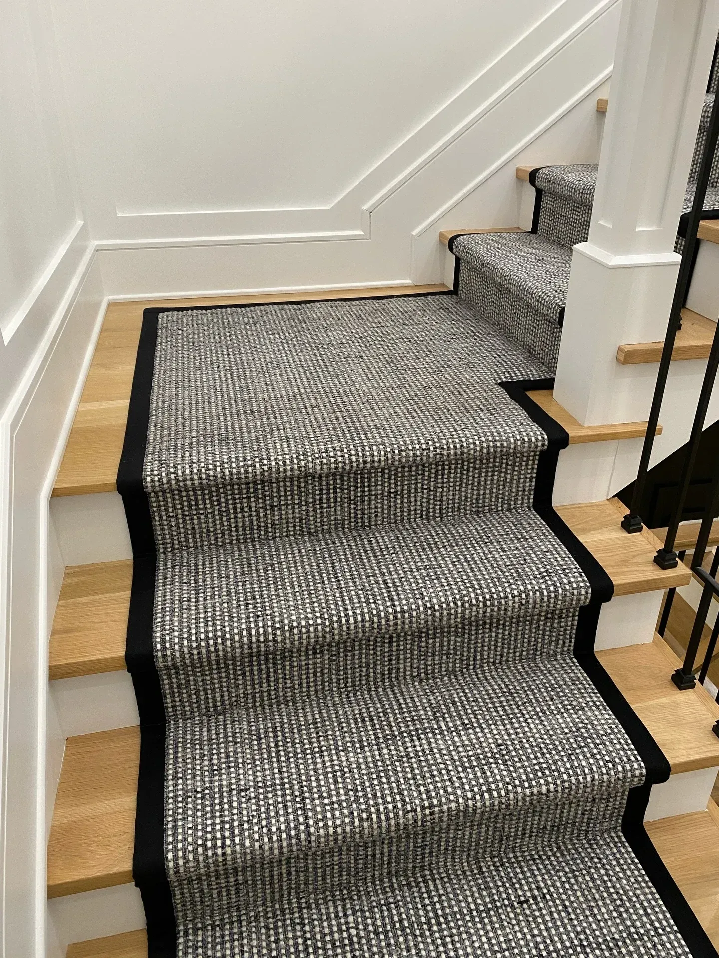 Carpeted staircase with black trim and white walls in a hallway