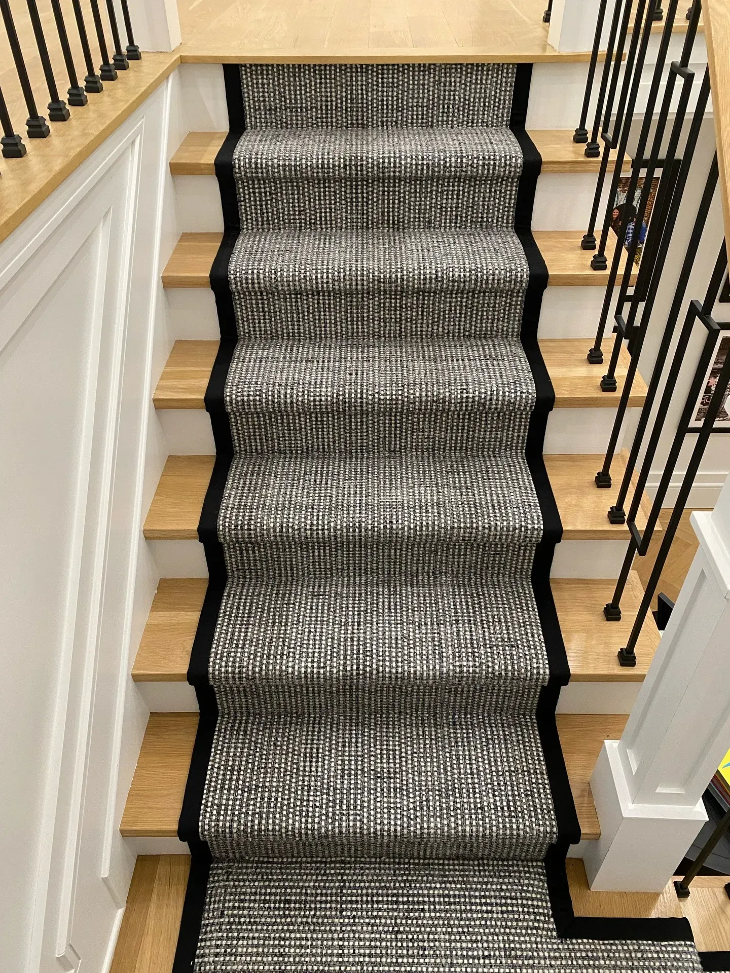 Black-and-white runner carpeted staircase with wooden steps and black iron railings in a home interior