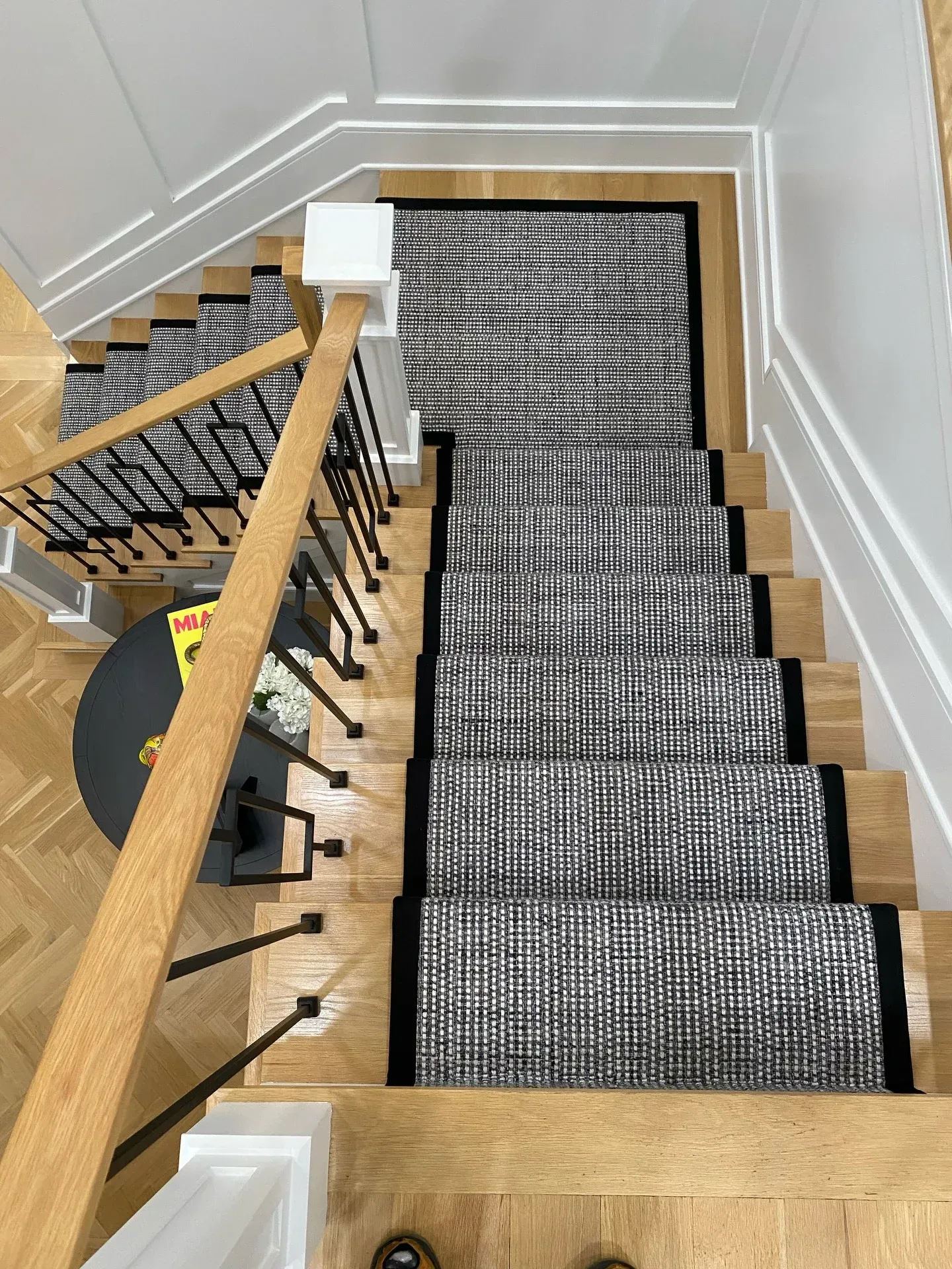 Staircase with black-and-white patterned runner carpet, wooden handrail, and light walls viewed from above