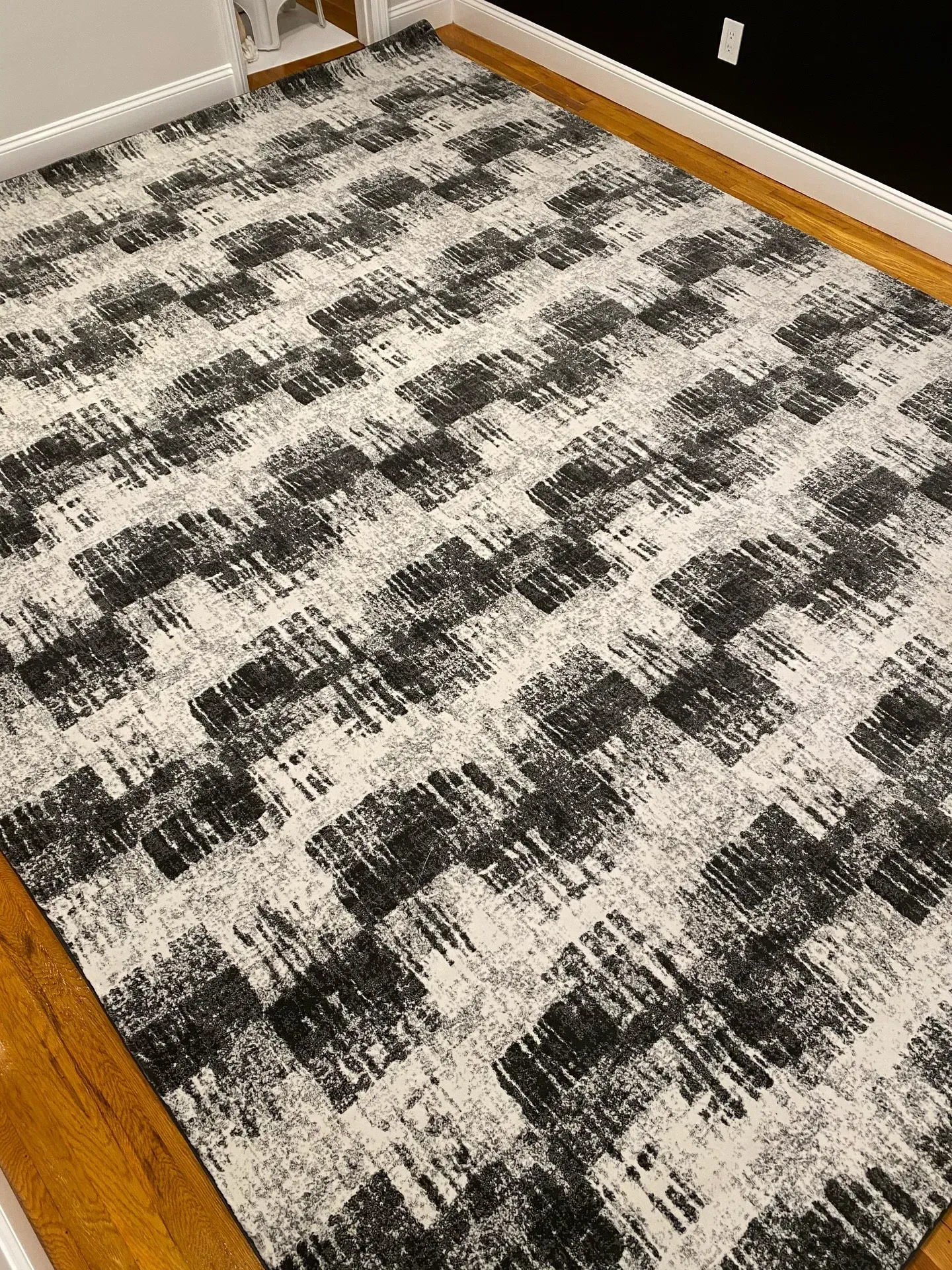Black, white, and gray patterned carpet in an empty room with hardwood edging and wall baseboards