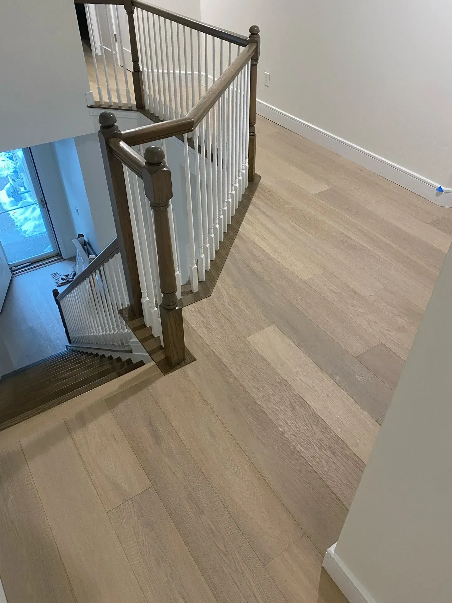 Staircase landing with white railings and light wood flooring beside a stairwell opening.