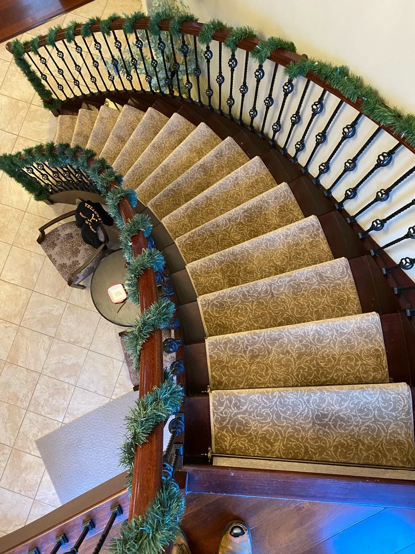 Curved staircase with beige carpet, dark railings, and green garland in a tiled interior foyer