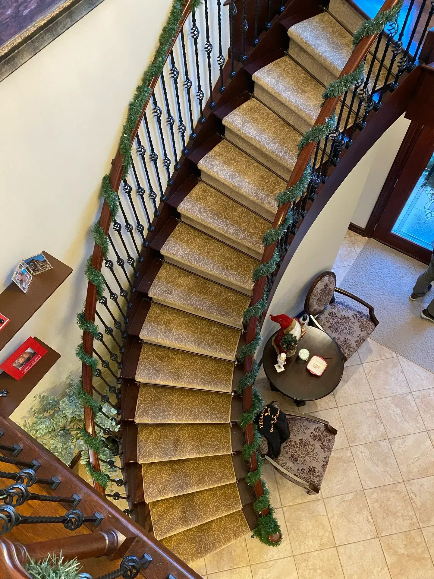 Curved indoor staircase with floral railings beside a tiled foyer and small round table
