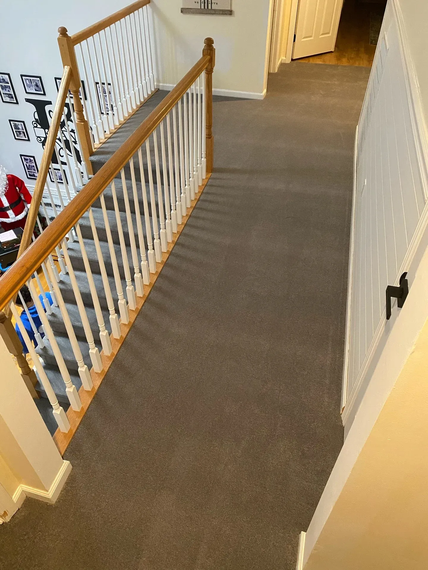 Carpeted upstairs hallway with wooden banister and white railing leading to a doorway.