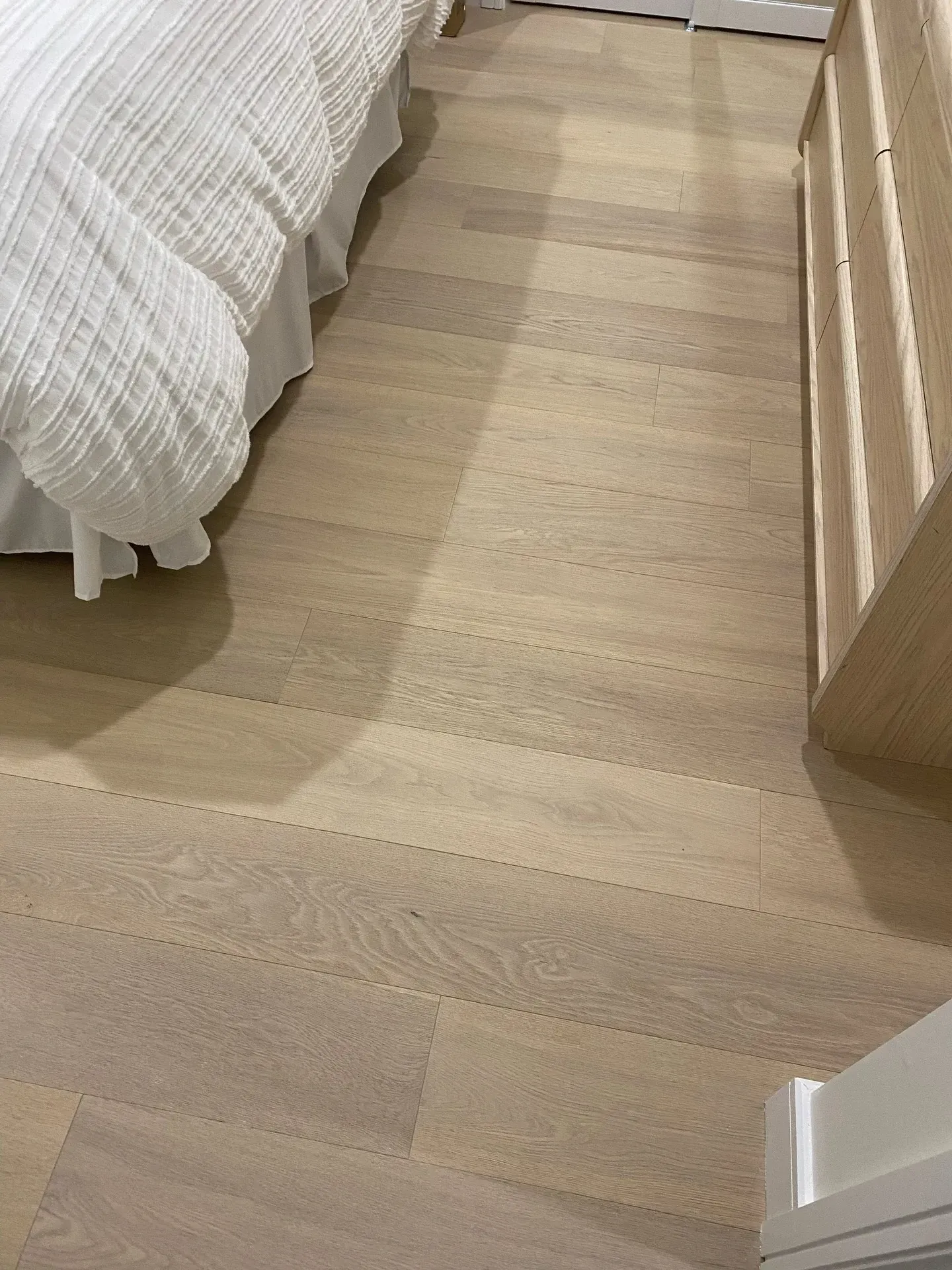 Light wood bedroom floor beside a bed with white bedding and a wooden dresser